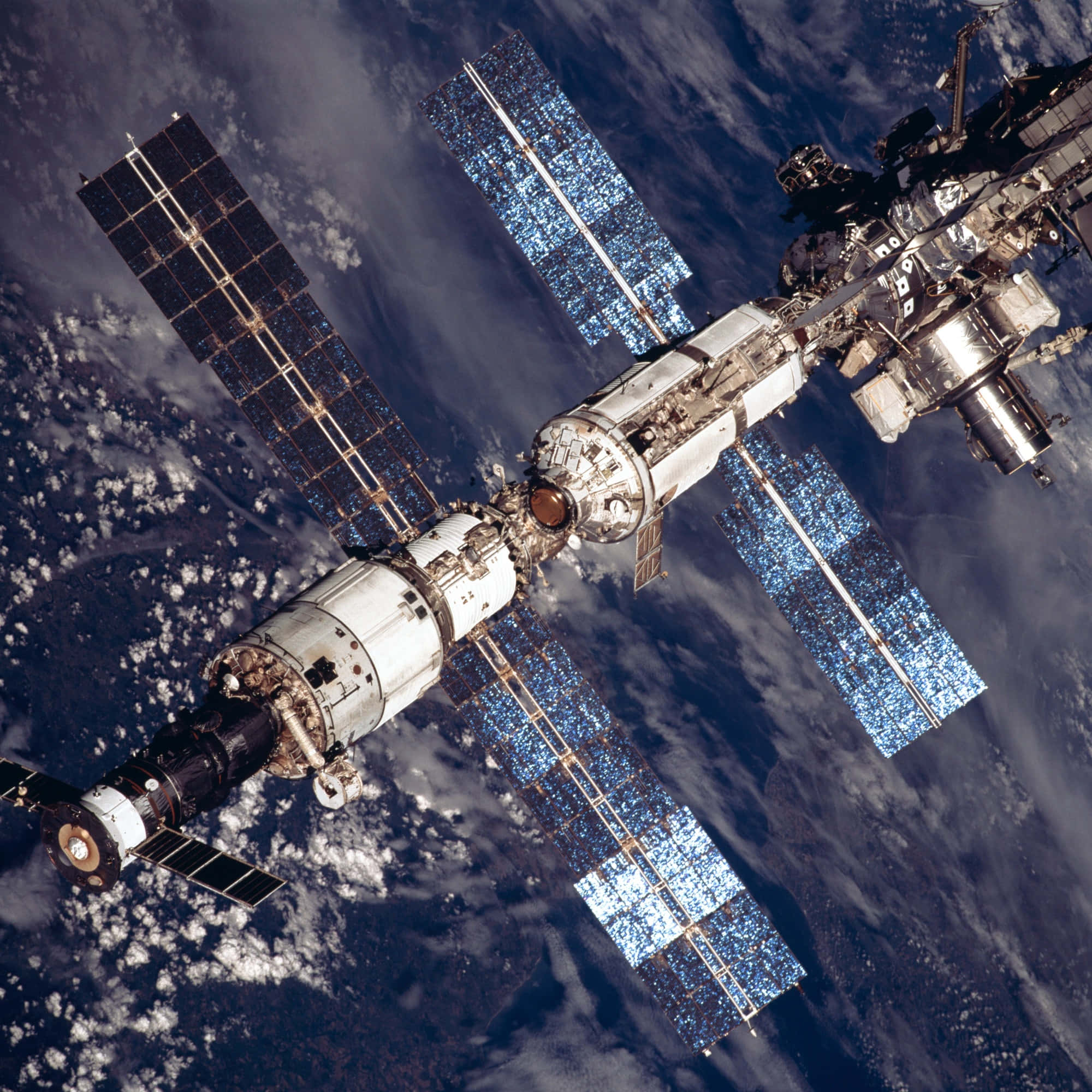NASA 動態圖片 桌布 壁紙 — 國際太空站的詳細視圖，太陽能板展開，漂浮在地球藍白雲層覆蓋的表面之上。