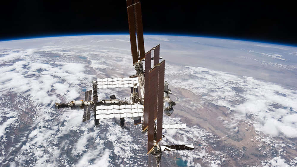 International Space Station 桌布 壁紙 — 國際太空站繞地球軌道運行，顯示下方有雲層和陸地的彎曲地平線。