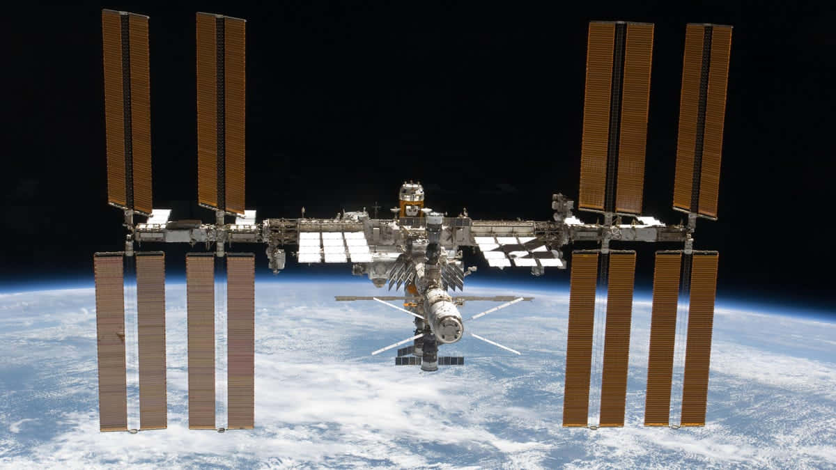 International Space Station 桌布 壁紙 — 國際太空站繞地球運行，太陽能板伸展在太空的漆黑中。