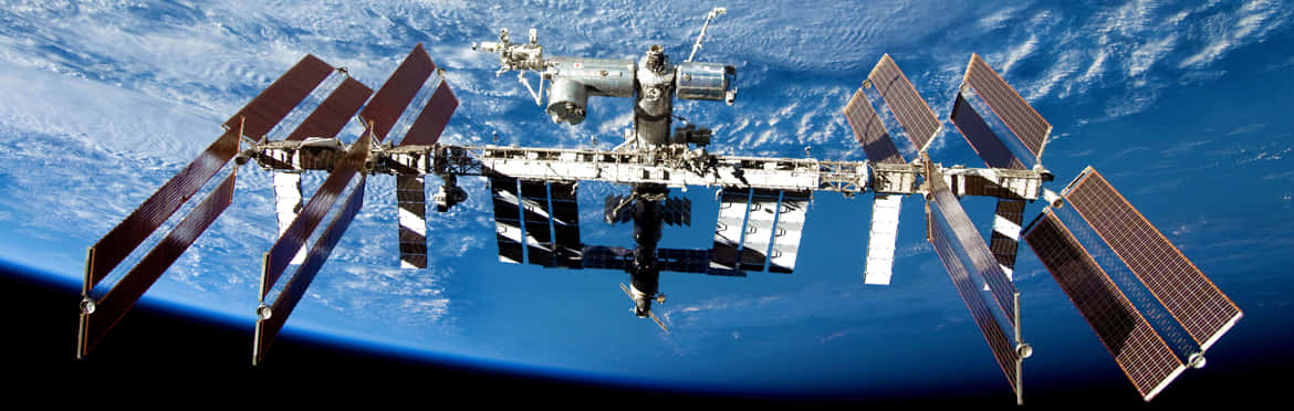 International Space Station 桌布 壁紙 — 國際太空站繞地球運行，太陽能板展開，背景是藍色海洋和白色雲層。