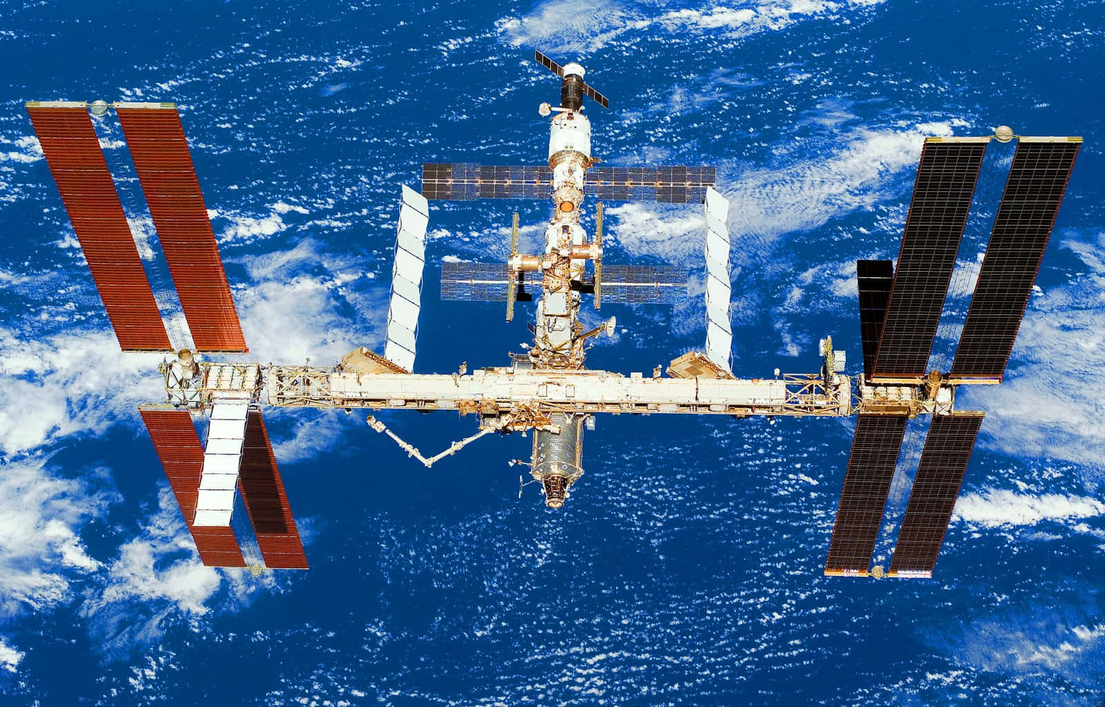 Iss 桌布 壁紙 — 國際太空站繞地球運行，太陽能板展開，背景是深藍色的海洋和白色的雲層。