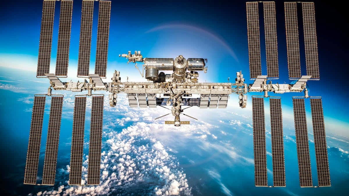 International Space Station 桌布 壁紙 — 國際太空站繞地球運行，太陽能板展開，背景是藍色行星和白色雲層。