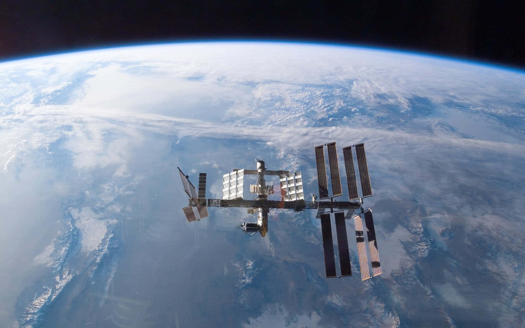 Space Technology 桌布 壁紙 — 國際太空站繞地球運行，顯示藍色海洋、白色雲層和黑色太空中的彎曲地平線。