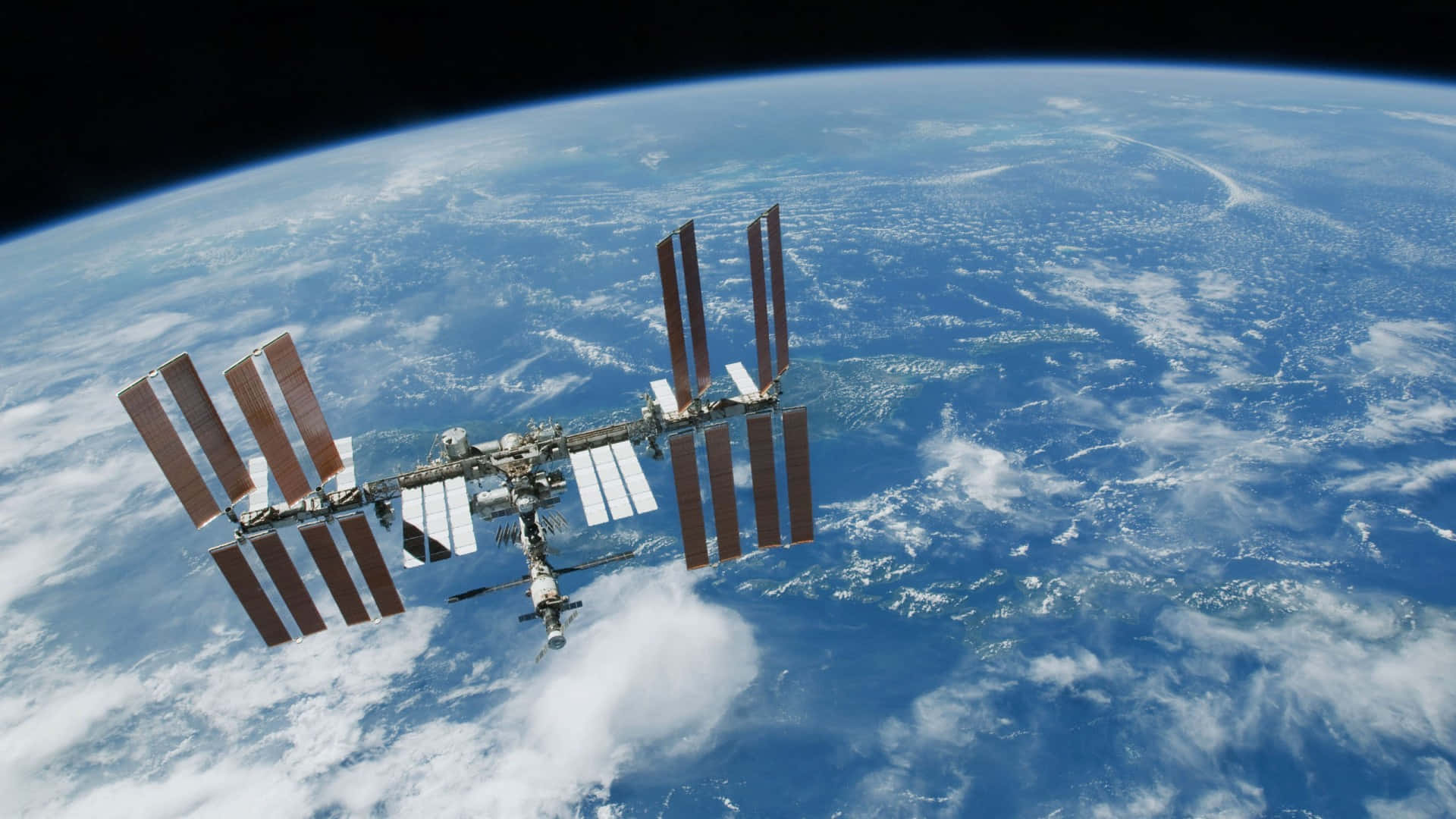 Iss 桌布 壁紙 — 國際太空站繞地球運行，顯示藍色海洋、白色雲朵和黑色太空中的彎曲地平線。
