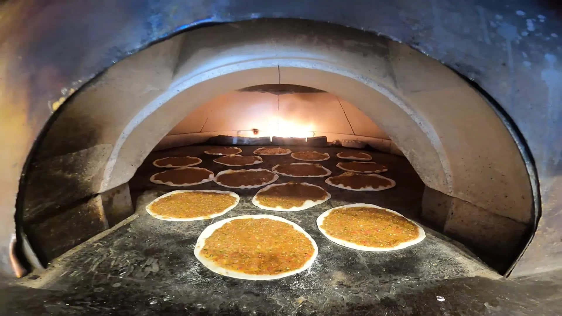 Bakery 桌布 壁紙 — 圓形扁麵包配金色配料在發光的石窯中烘烤，帶有溫暖的環境光。