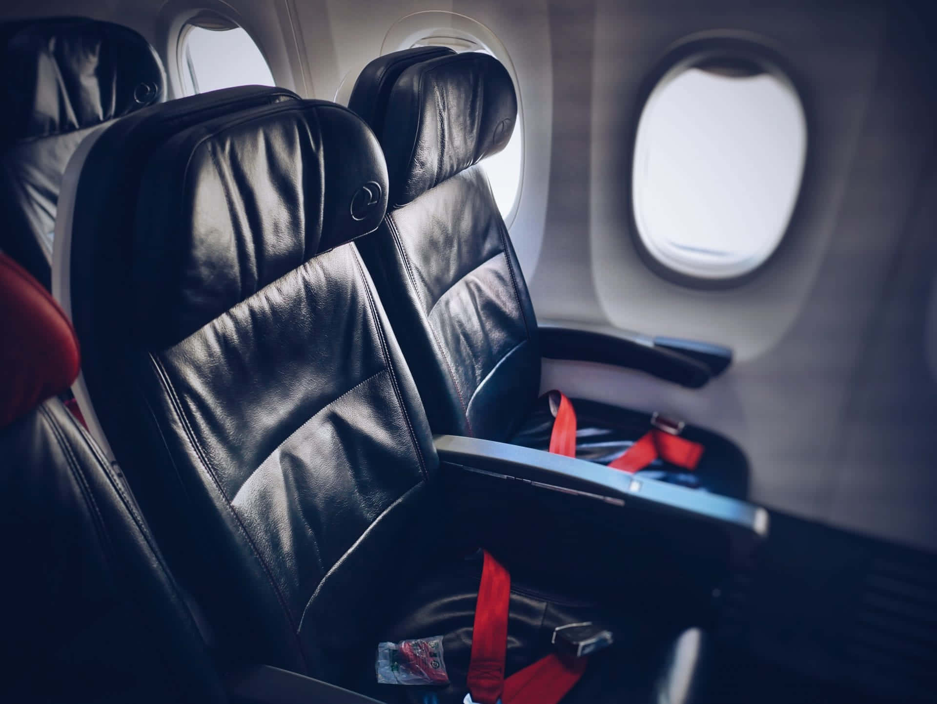 seat 桌布 壁紙 — 圓窗附近柔和機艙燈光下黑色皮革飛機座椅配紅色安全帶的特寫。
