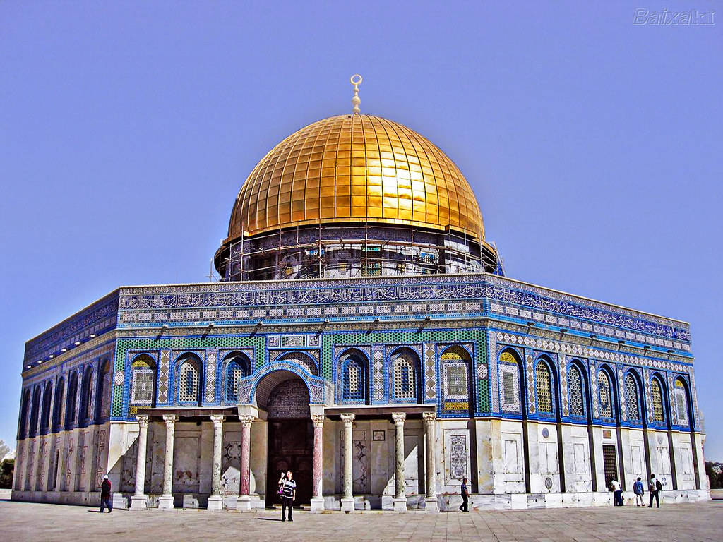 muslim 桌布 壁紙 — 圓頂清真寺在清澈藍天下閃耀金光，精緻的藍色瓷磚工藝和遊客在其宏偉入口處。