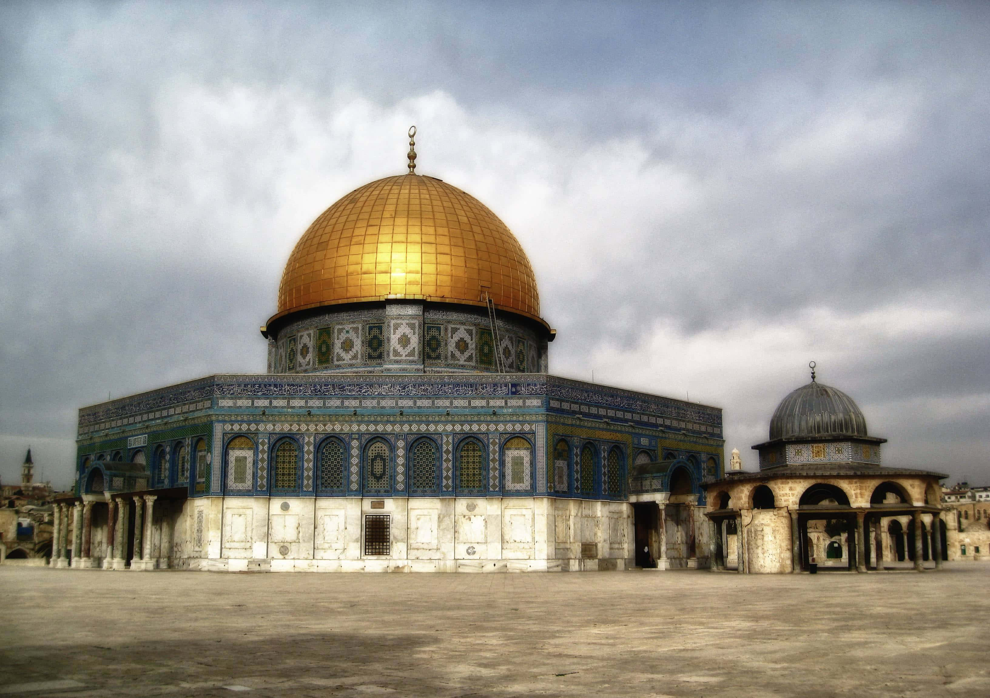 Israel 桌布 壁紙 — 圓頂清真寺在陰天天空下閃耀金光，其複雜的藍色瓷磚與石頭廣場形成對比。