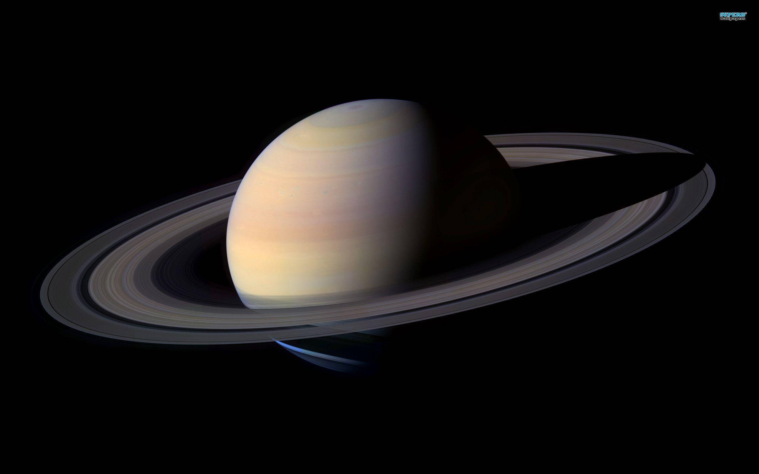 土星 桌布 壁紙 — 土星在虛空中柔和地發光，其標誌性的環在宇宙黑暗中投下長長的陰影。