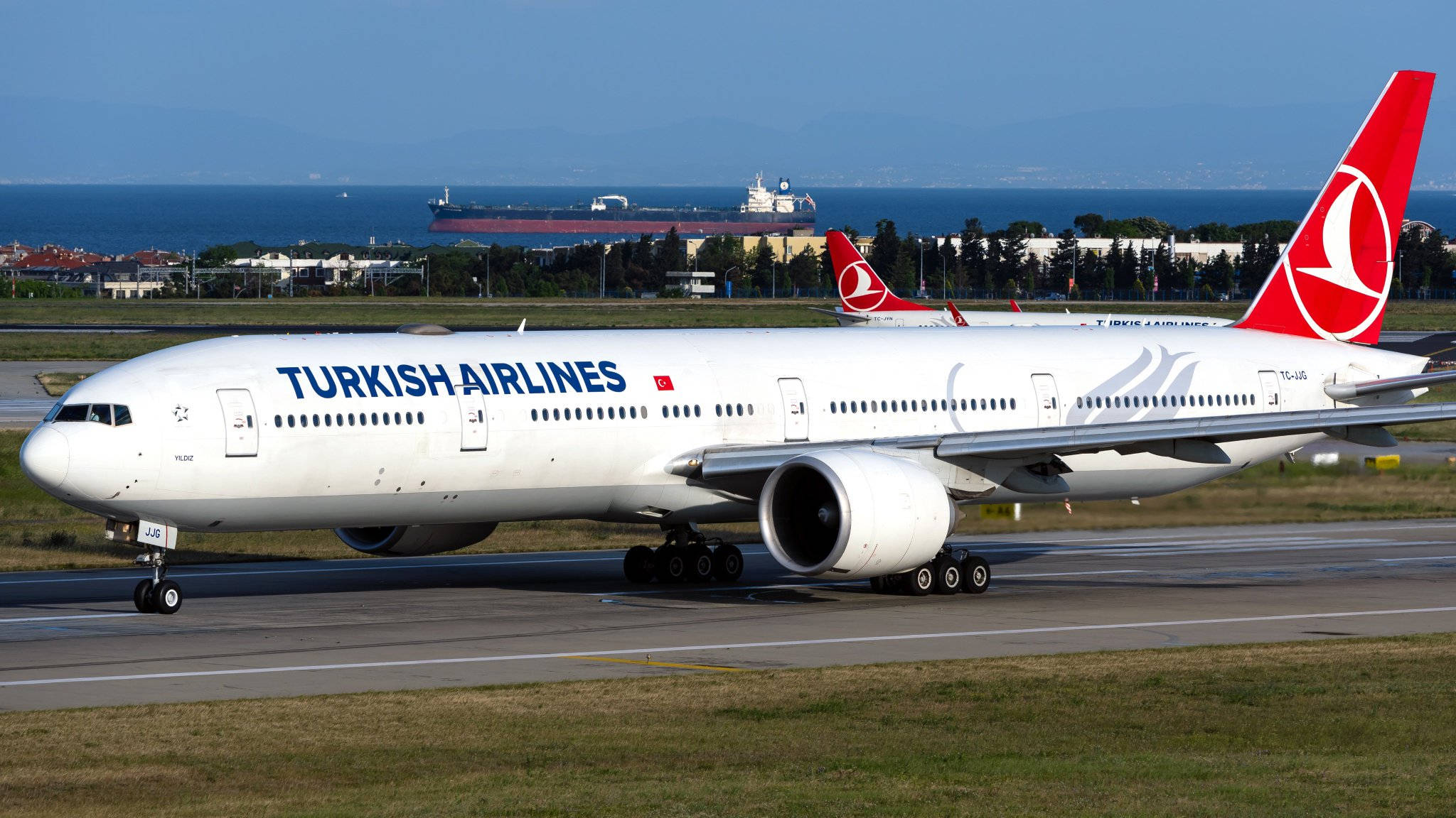 飛機 桌布 壁紙 — 土耳其航空波音777在跑道上滑行，遠方海洋上可見一艘貨船。