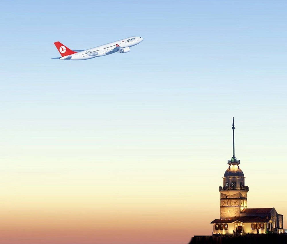 風景 桌布 壁紙 — 土耳其航空飛機在日落時分飛過燈光璀璨的少女塔，背景是漸變色的天空。
