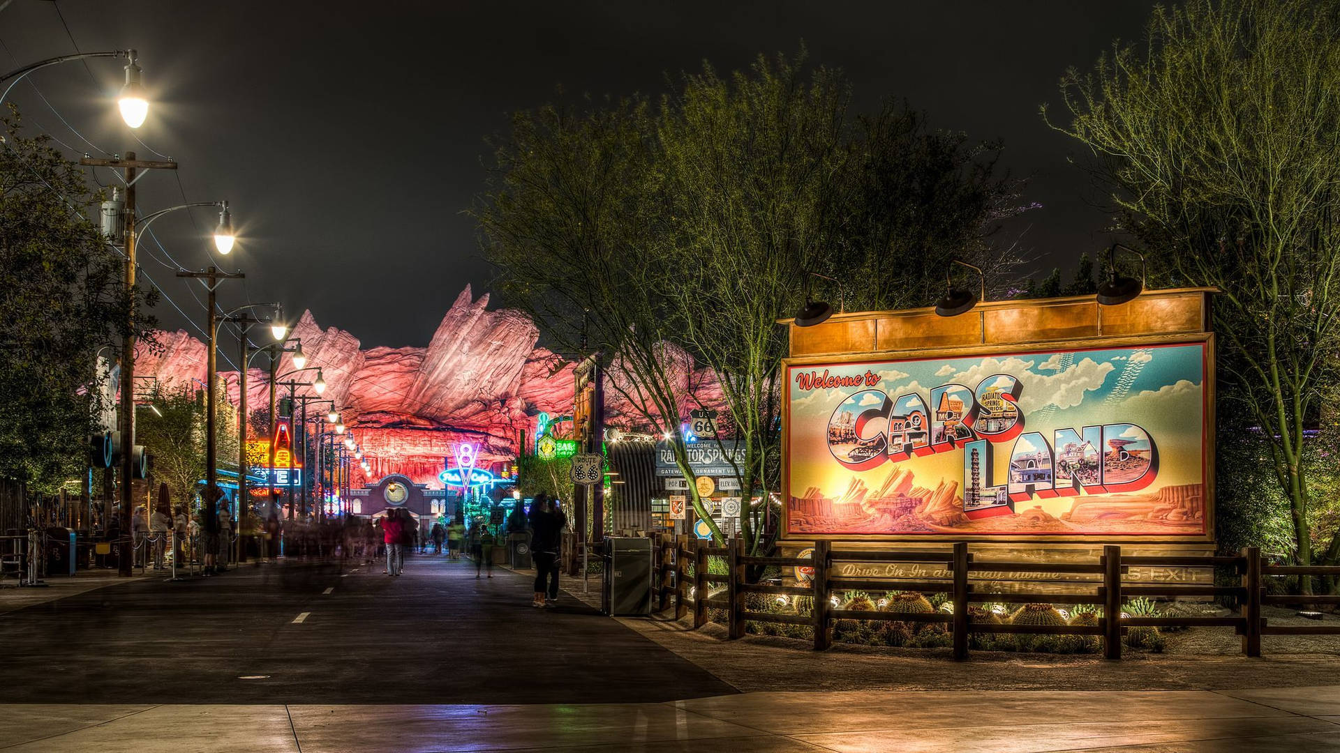 加州 桌布 壁紙 — 在 Cars Land 一條充滿活力的夜間街道，有發光的霓虹燈牌和一個大型彩色歡迎牌，在黑暗的天空下。