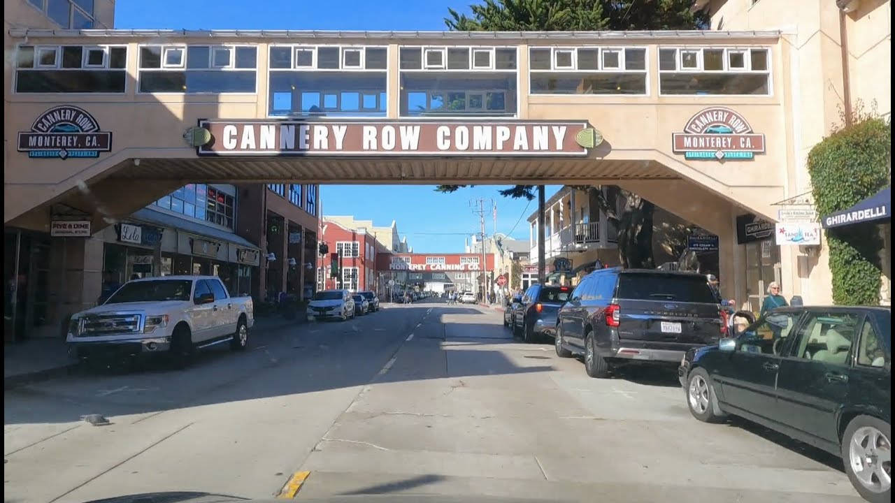 Road 桌布 壁紙 — 在Cannery Row Company行人天橋下的陽光街景，路邊停有汽車和商店門面。