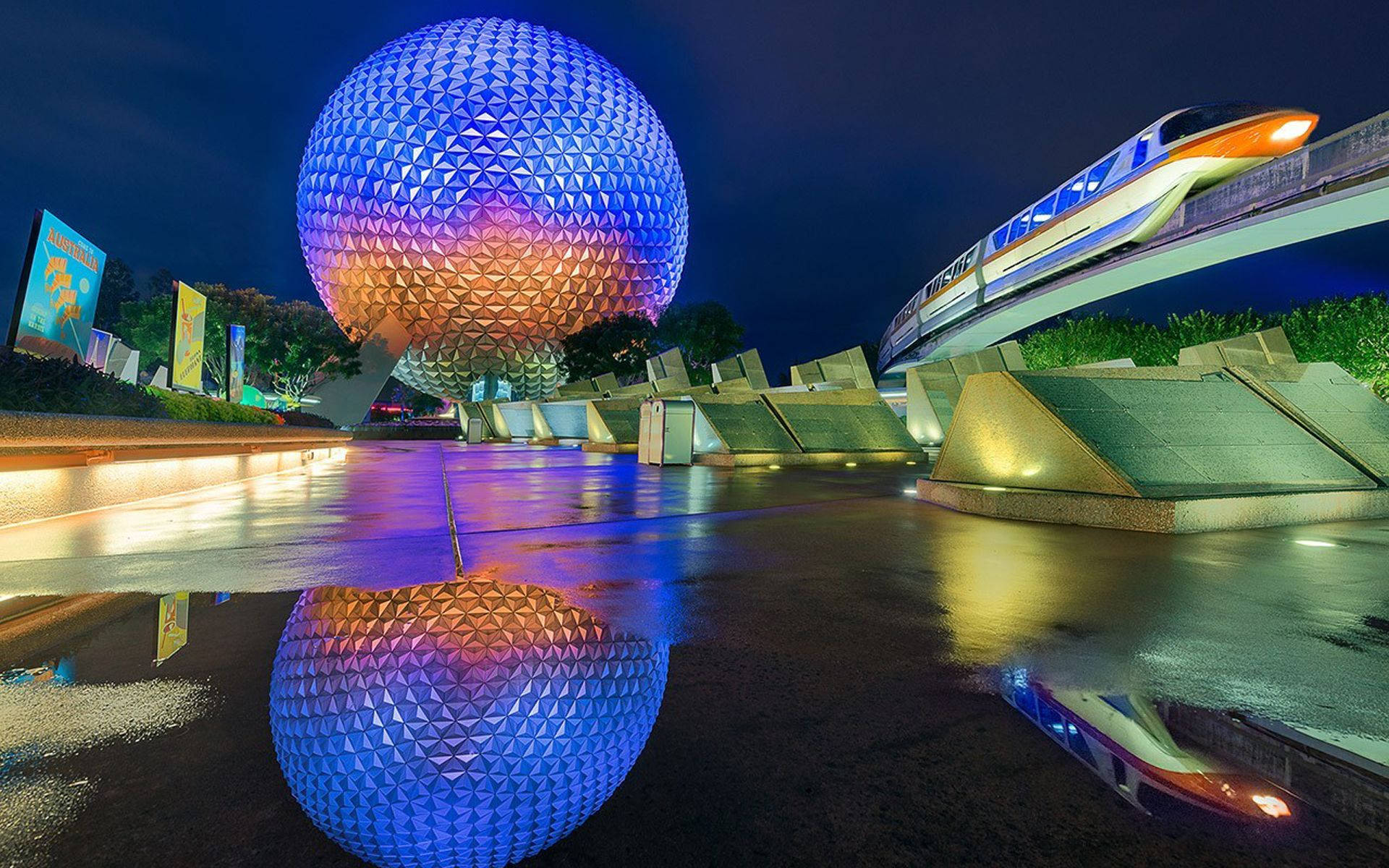 彩色動圖 桌布 壁紙 — 在Epcot，一個發光的測地線球體和單軌列車在漆黑的夜空下倒映在濕漉漉的路面上。