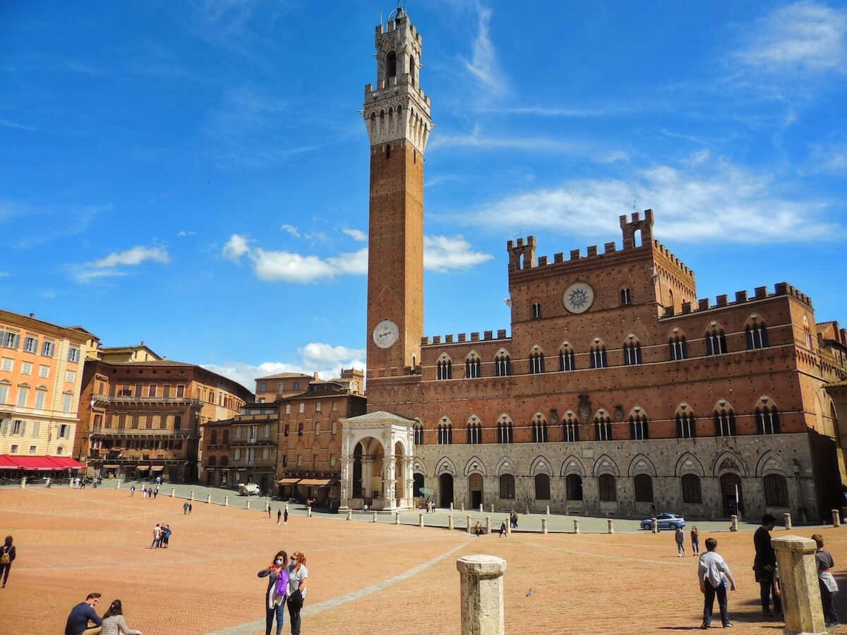 Brick 桌布 壁紙 — 在Piazza del Campo陽光明媚的一天，標誌性的Torre del Mangia和Palazzo Pubblico聳立在陶土廣場上的遊客之上。