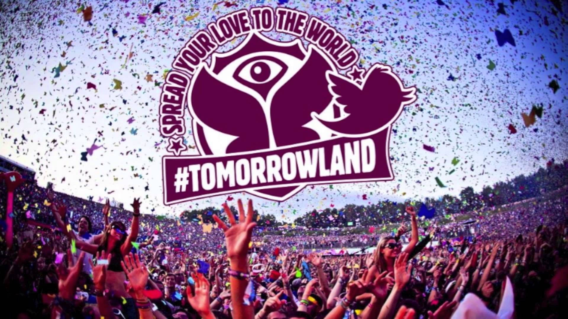 明日世界 桌布 壁紙 — 在Tomorrowland音樂節上，充滿活力的人群在灑滿彩色紙屑和活動標誌性標誌的天空下舉起雙手。