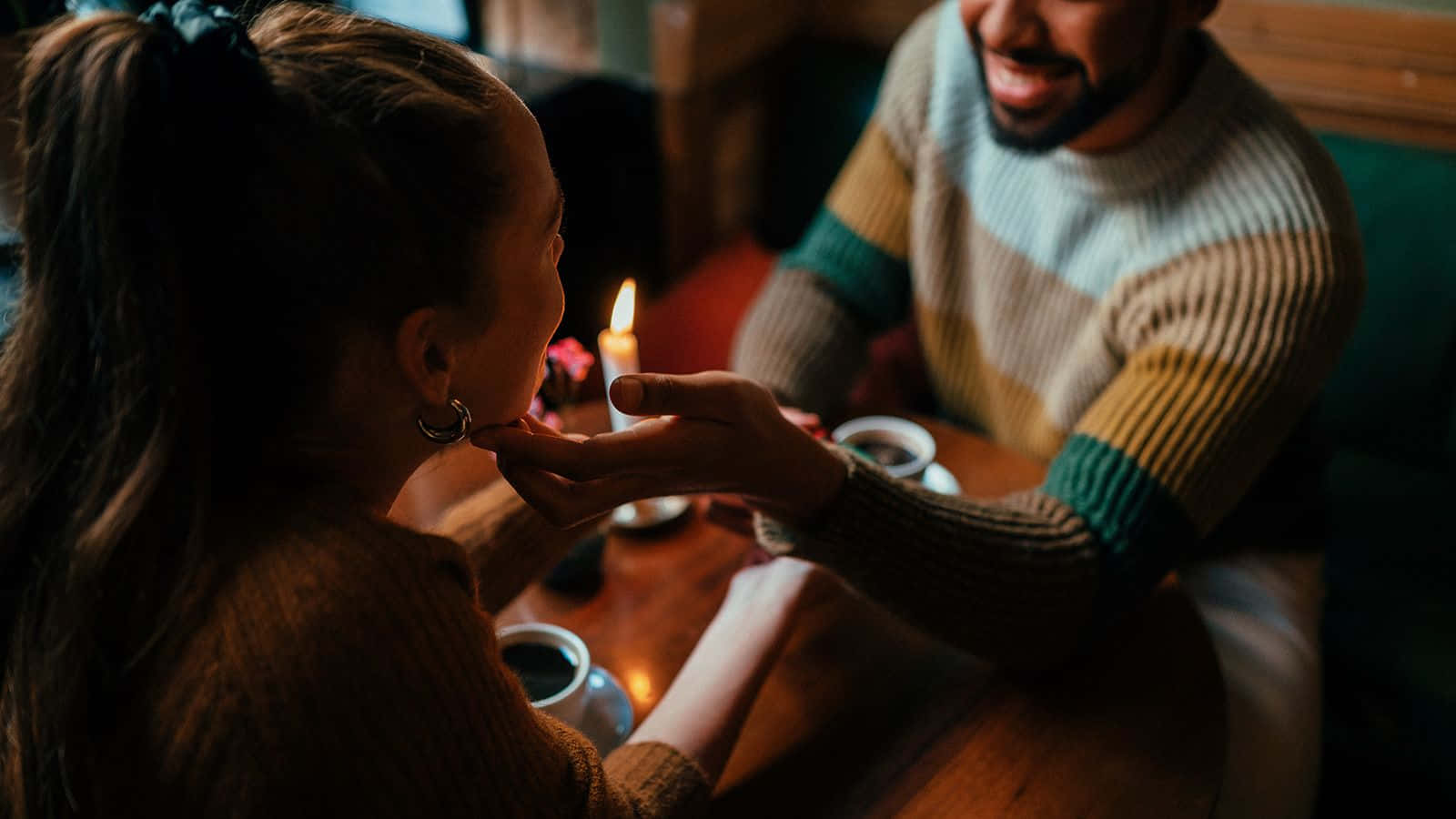 愛心 桌布 壁紙 — 在一個溫暖舒適、燭光搖曳的咖啡館裡，一名男子輕柔地餵一名女子吃一口食物。