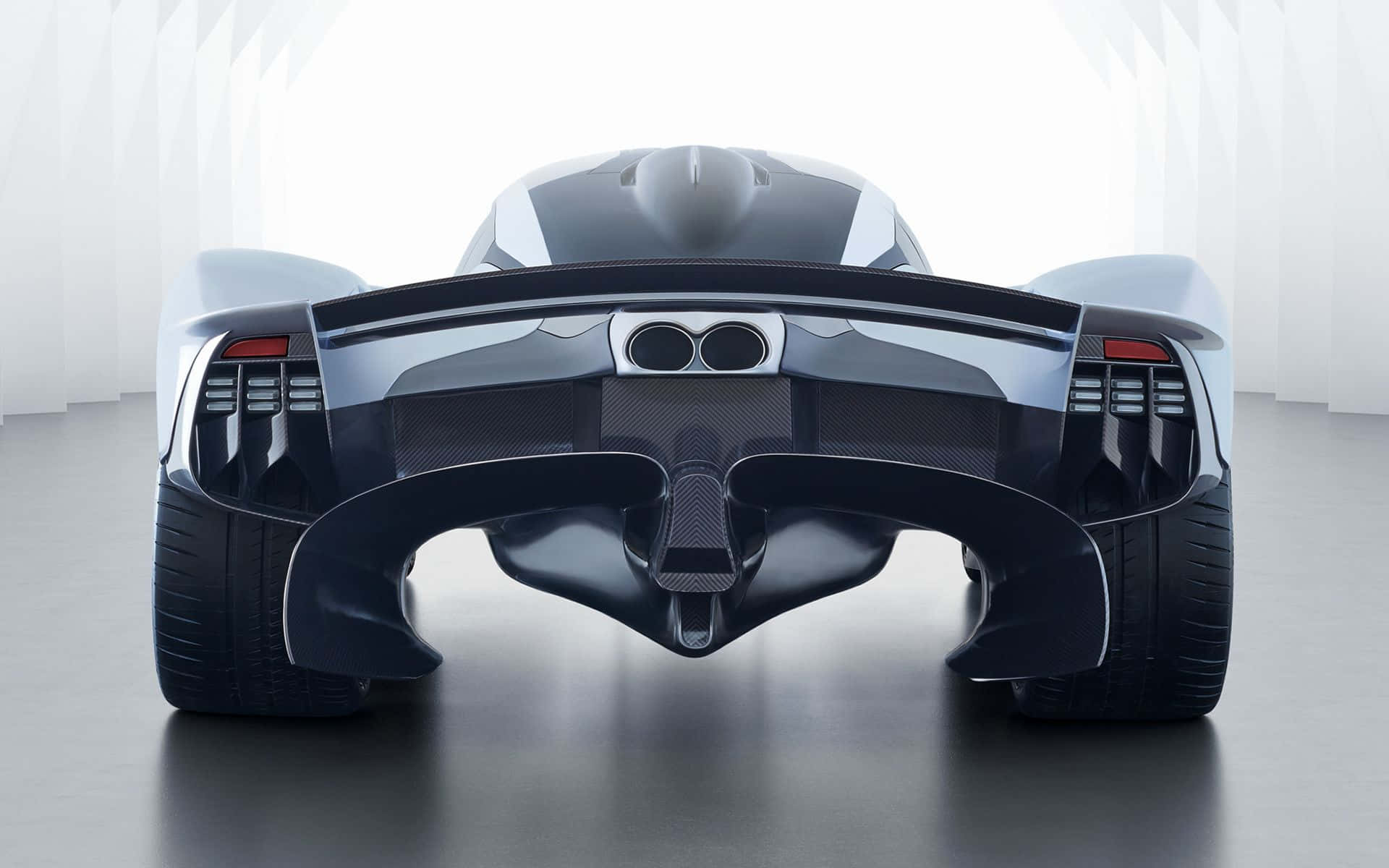 Aston Martin Valkyrie 桌布 壁紙 — 在一個簡約的工作室中，從後方觀看一輛時尚的未來主義跑車，工作室有明亮的白色牆壁和反光地板。