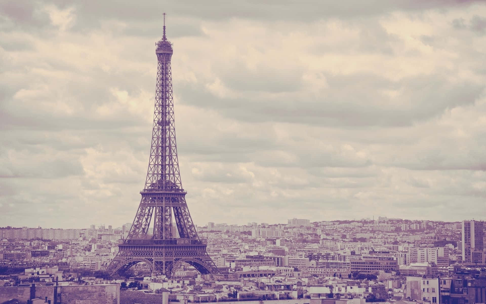 Paris Desktop 桌布 壁紙 — 在一張復古色調的照片中，艾菲爾鐵塔在陰雲密佈的天空下，聳立在廣闊的巴黎城市景觀之上。