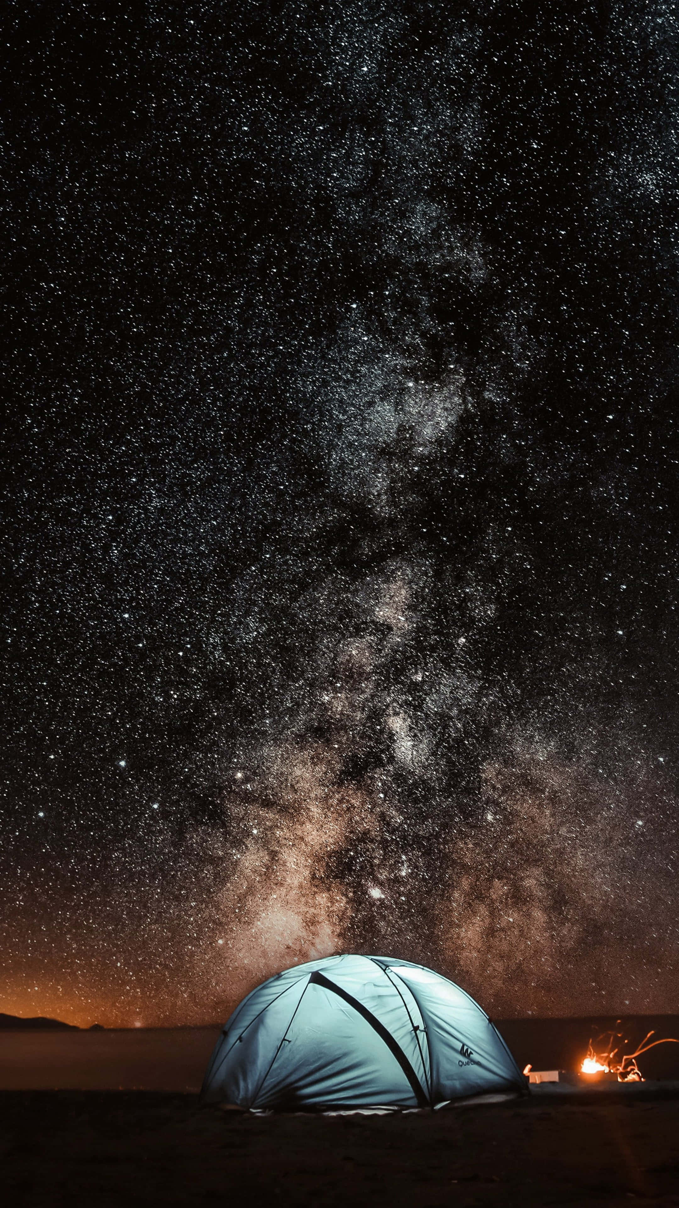 Starry Sky 桌布 壁紙 — 在令人驚嘆的星空下，一個發光的藍色帳篷，銀河在營火上拱起。