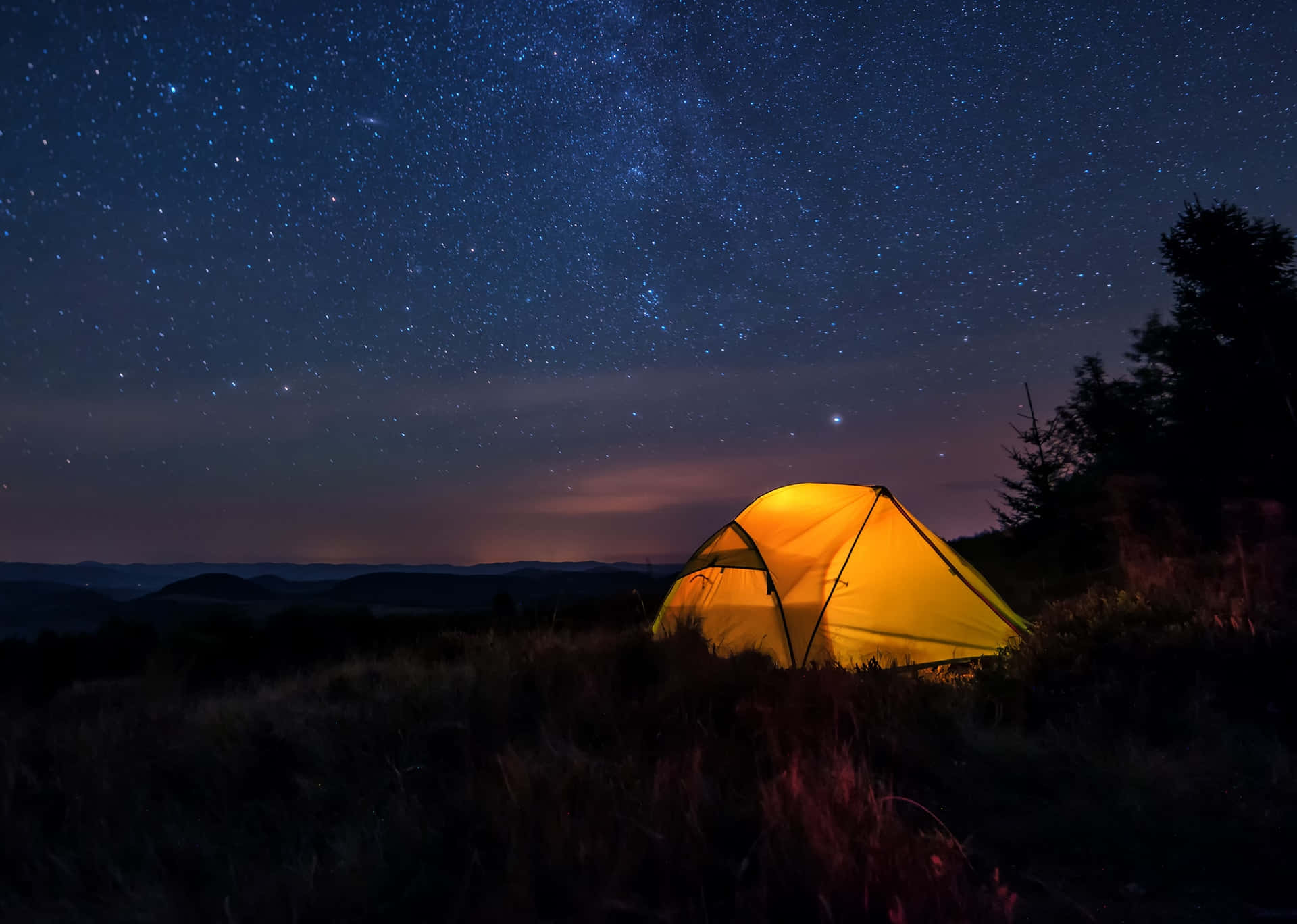 Camping 桌布 壁紙 — 在令人驚嘆的星空下，草地上有一個發光的黃色帳篷，銀河系清晰可見。