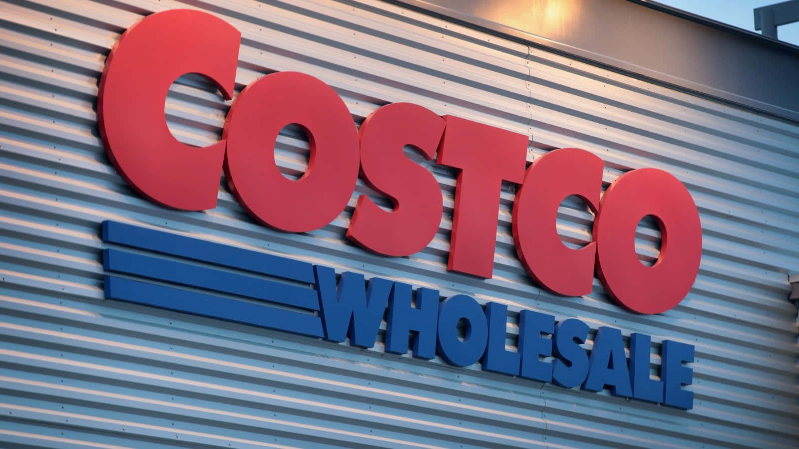 Costco 桌布 壁紙 — 在傍晚光線下，安裝在波紋金屬壁板上的大膽紅色和藍色Costco Wholesale標誌。