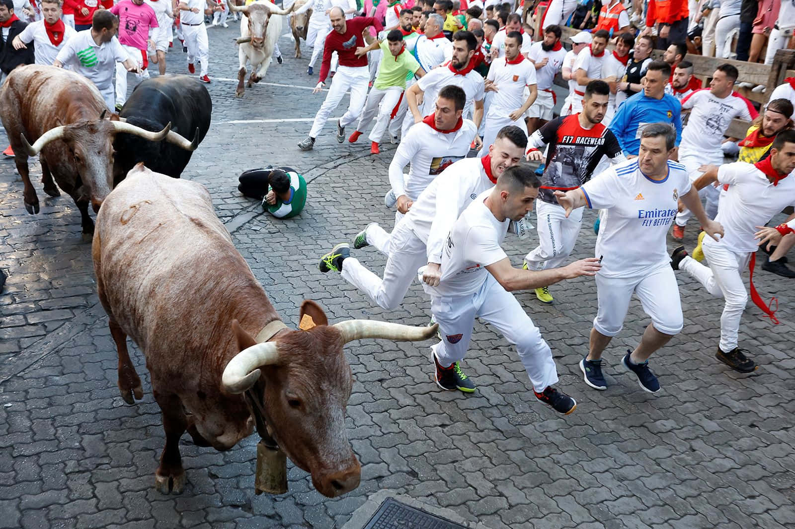 bull 桌布 壁紙 — 在傳統節日期間，身穿白衣的男子在鵝卵石街道上緊急奔跑，經過衝鋒的公牛。