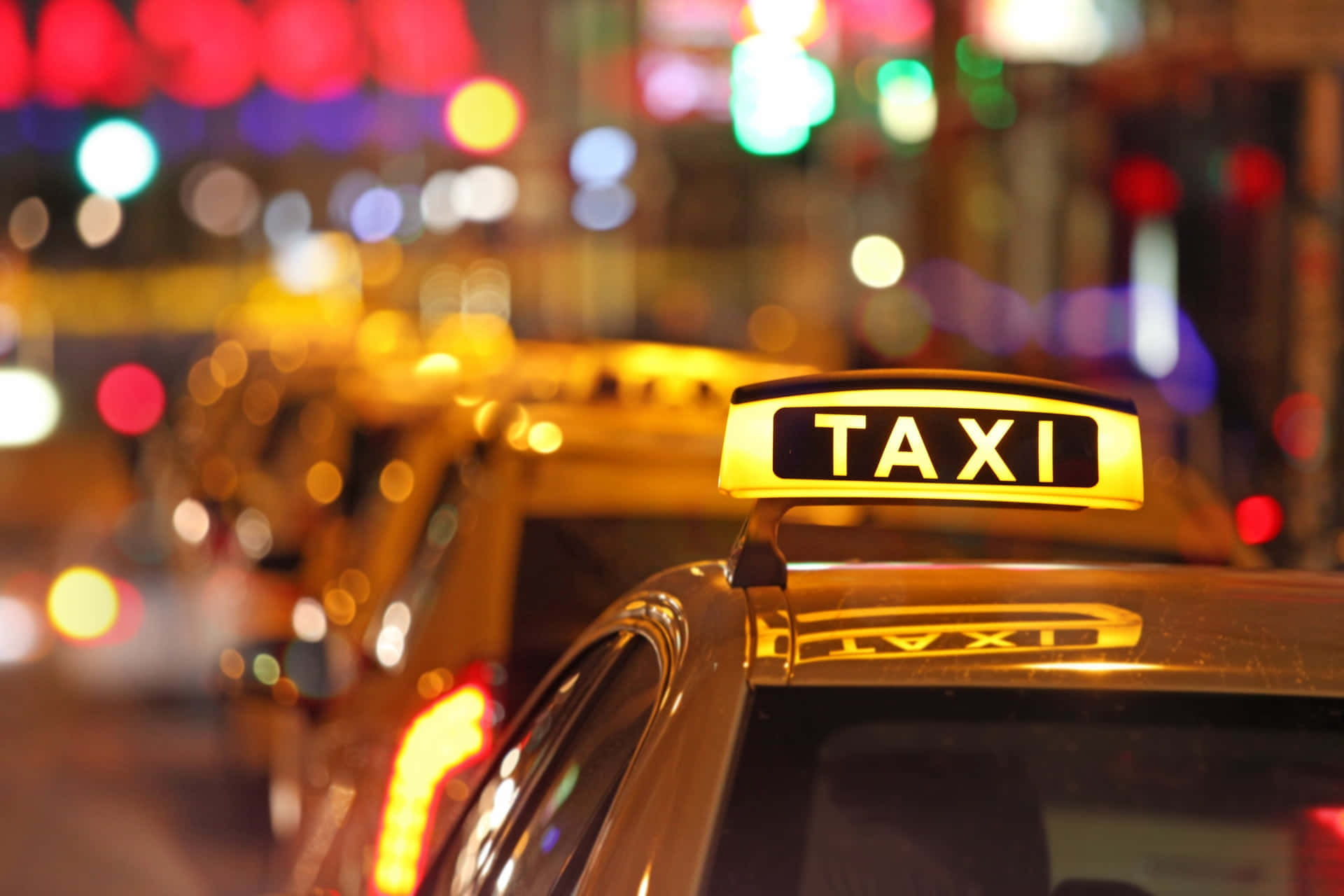 Yellow Cab 桌布 壁紙 — 在充滿活力的散景燈光城市夜景中，一輛計程車頂上發光的黃色計程車標誌。