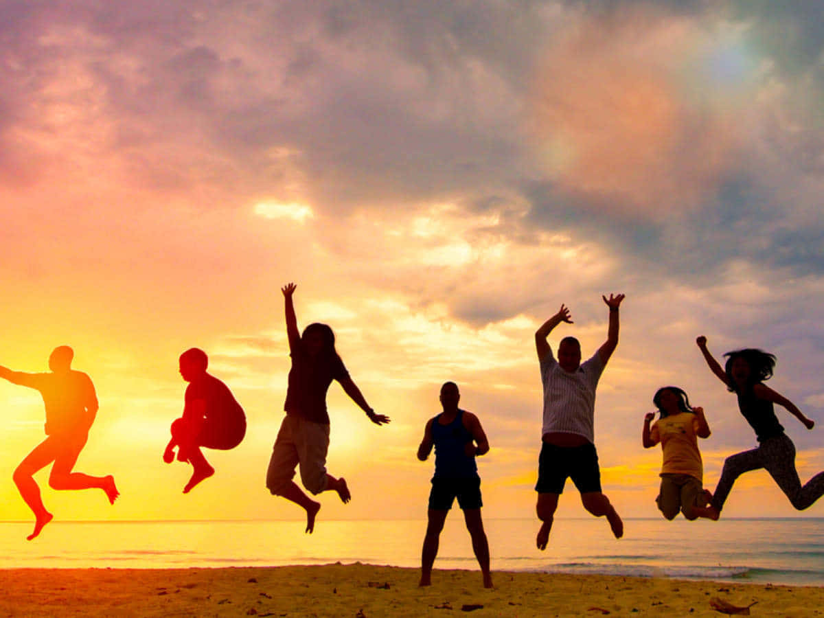 Friendship 桌布 壁紙 — 在充滿活力的橙色和粉紅色天空下，海灘上歡樂跳躍的人們的剪影。