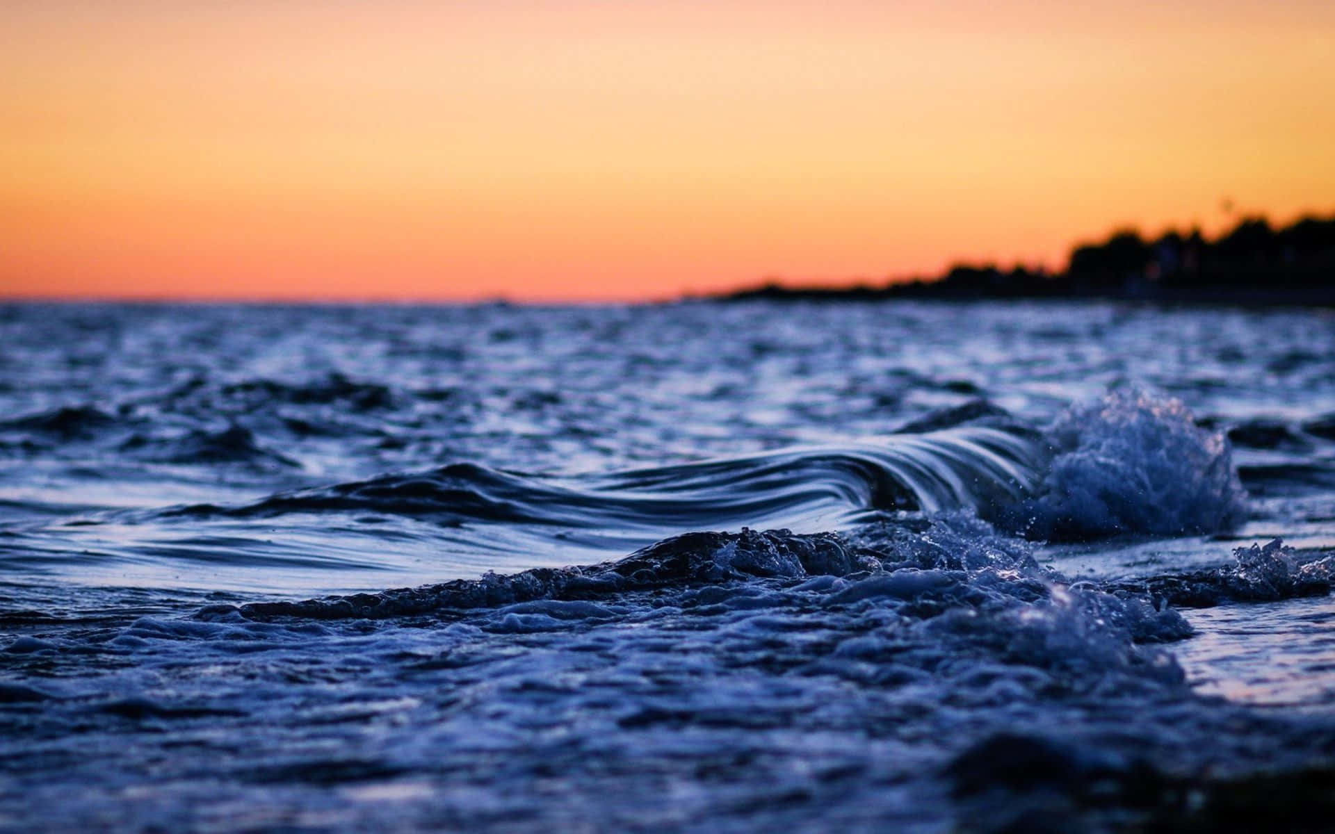 Ocean Waves 桌布 壁紙 — 在充滿活力的橙色和粉紅色日落天空下，海浪沖上岸邊。