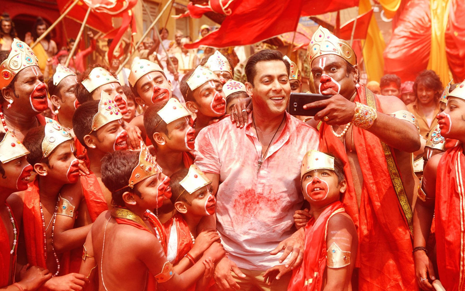 Salman Khan 桌布 壁紙 — 在充滿活力的灑紅節期間，一位身穿粉紅色襯衫的快樂男子與滿身紅色粉末的孩子們自拍。