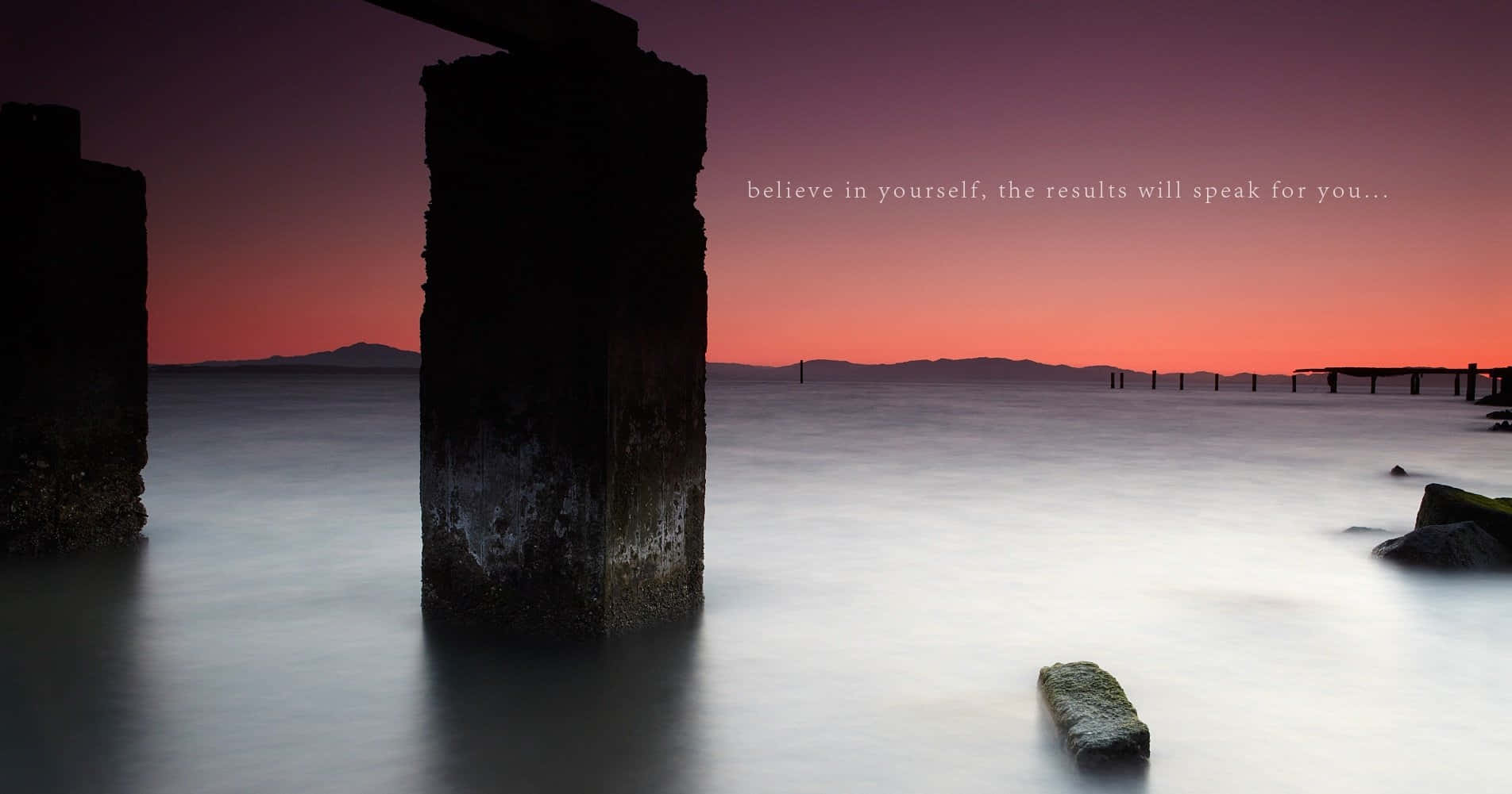 Motivation 桌布 壁紙 — 在充滿活力的粉紅色和紫色日落天空下，剪影的碼頭樁柱從平靜的水面升起。