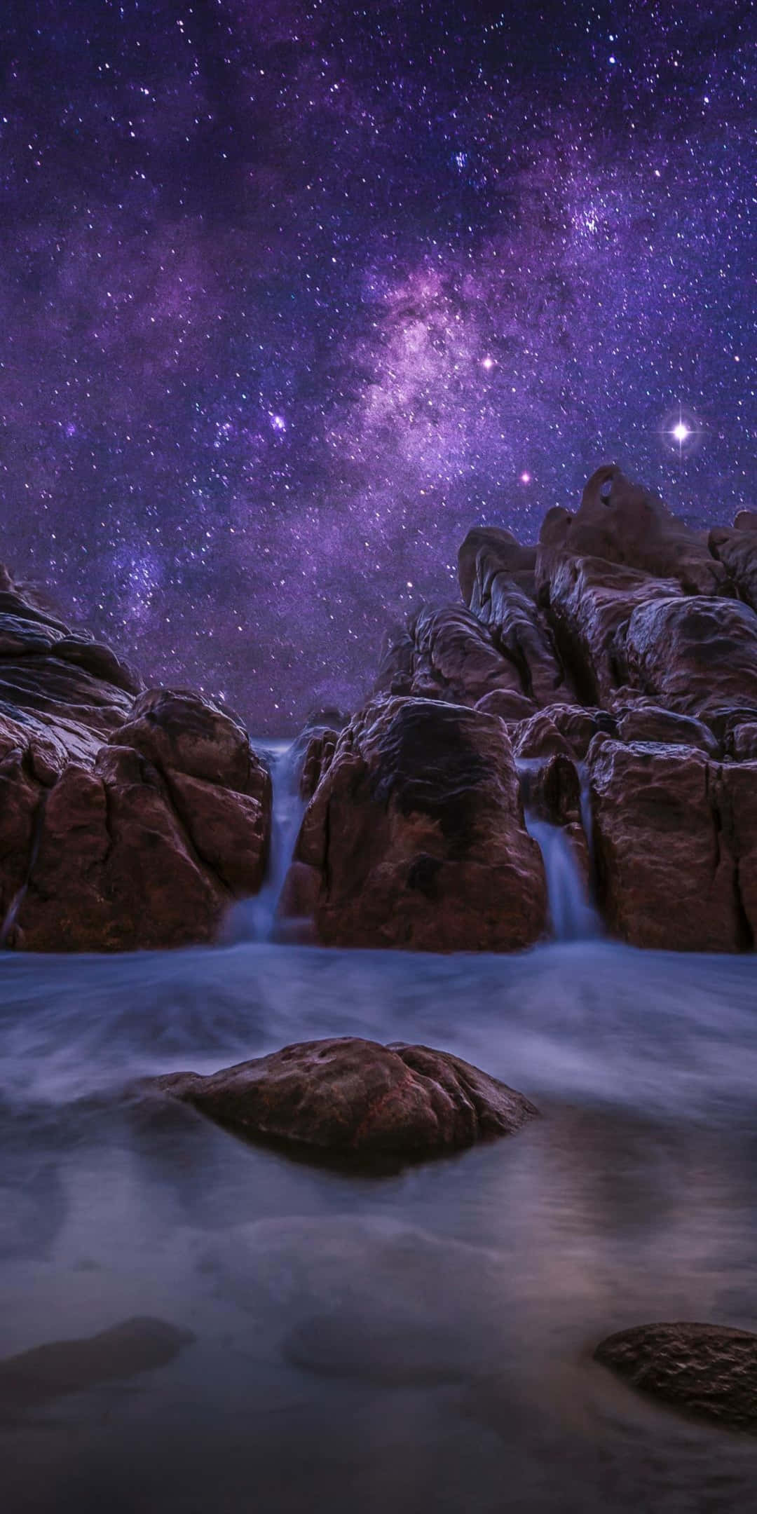 自然 桌布 壁紙 — 在充滿銀河系的充滿活力的紫色星空下，瀑布在崎嶇的岩石之間傾瀉而下。
