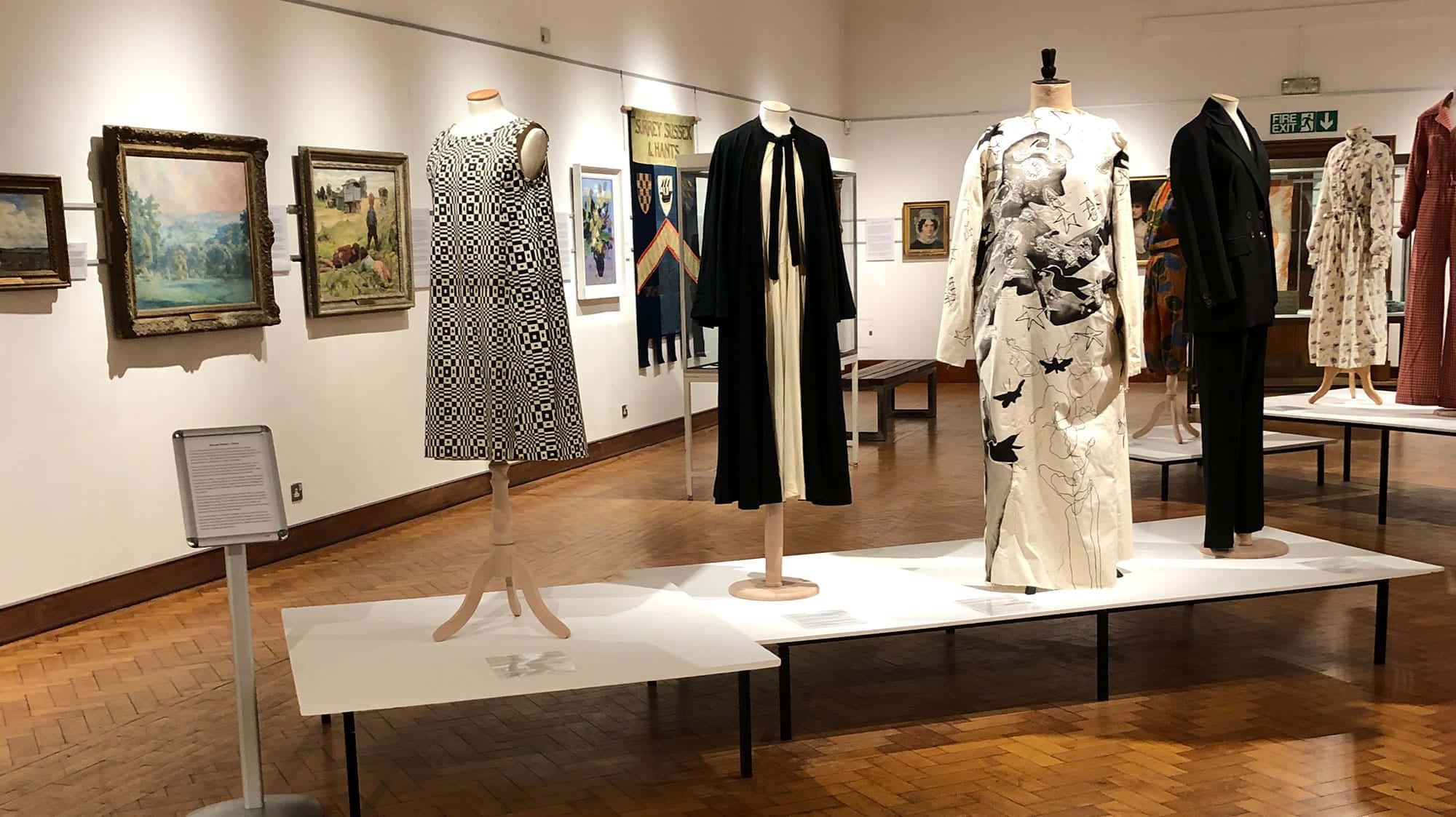 Museum 桌布 壁紙 — 在光線充足的博物館畫廊中，人體模型上展示的優雅復古服裝，牆上掛著帶框的畫作。