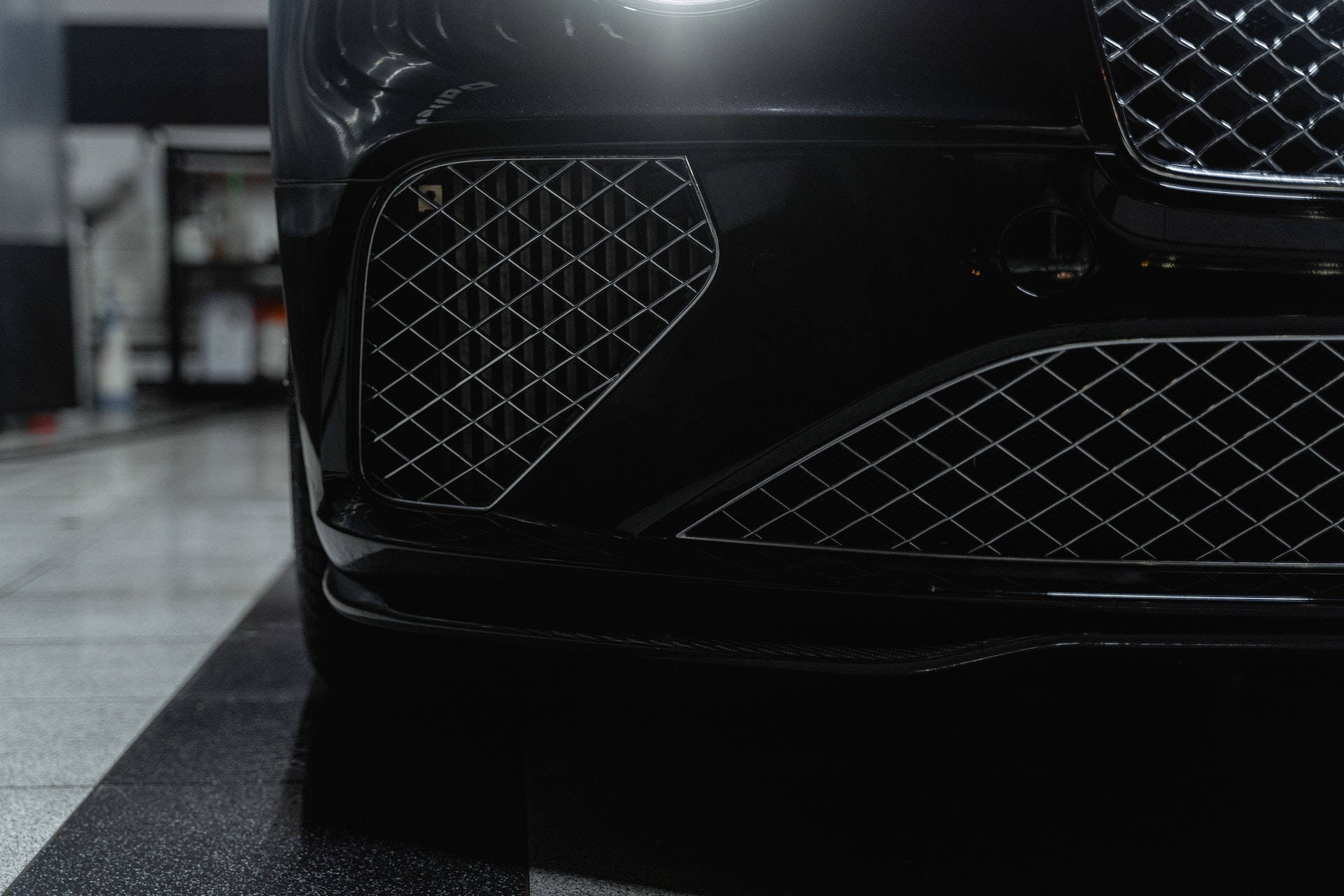 Bentley Cars 桌布 壁紙 — 在光線昏暗、地板反光的車庫中，一輛時尚黑色豪華汽車的前格柵和保險桿的特寫。