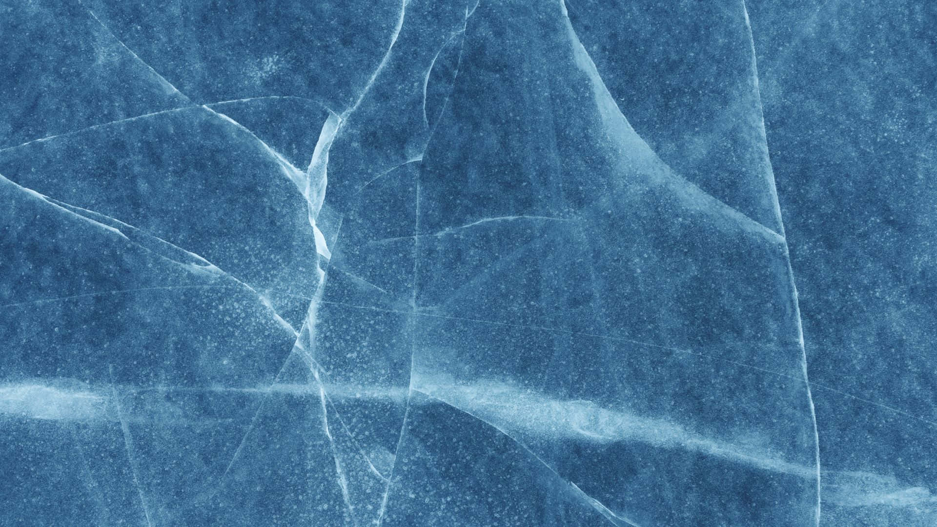Blue Marble 桌布 壁紙 — 在冷色調燈光下，裂開的藍色冰塊特寫，帶有複雜的白色裂縫和微妙的雪粒。
