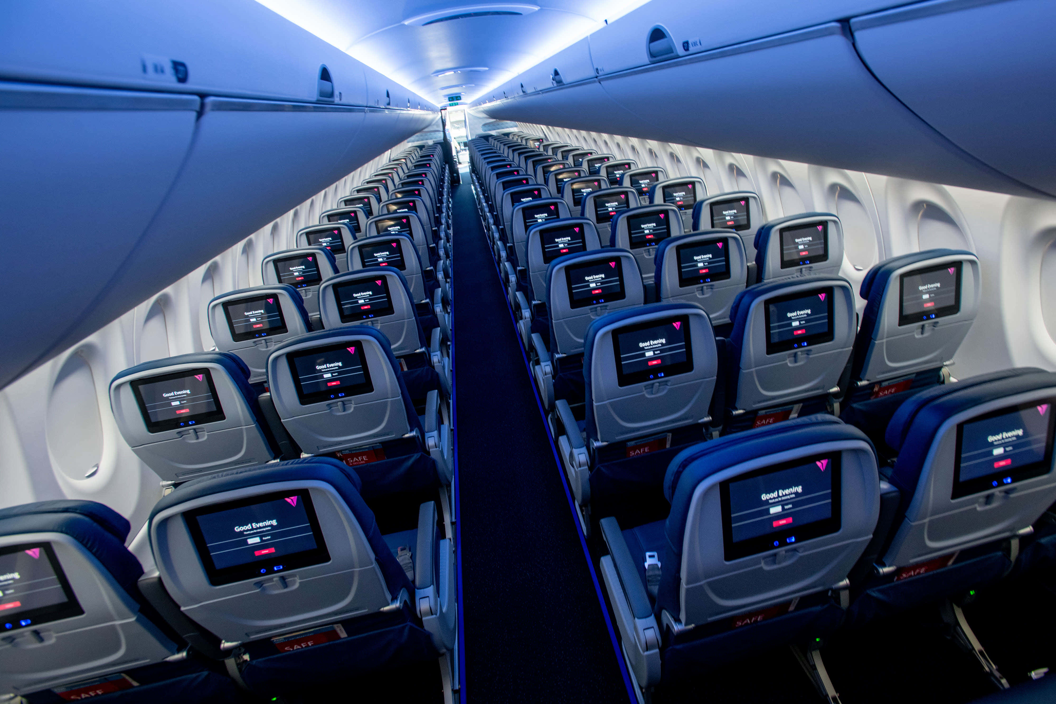 seat 桌布 壁紙 — 在冷色調藍色機艙燈光下，飛機座位排之間的一條長長通道，亮起的螢幕顯示「晚安」。