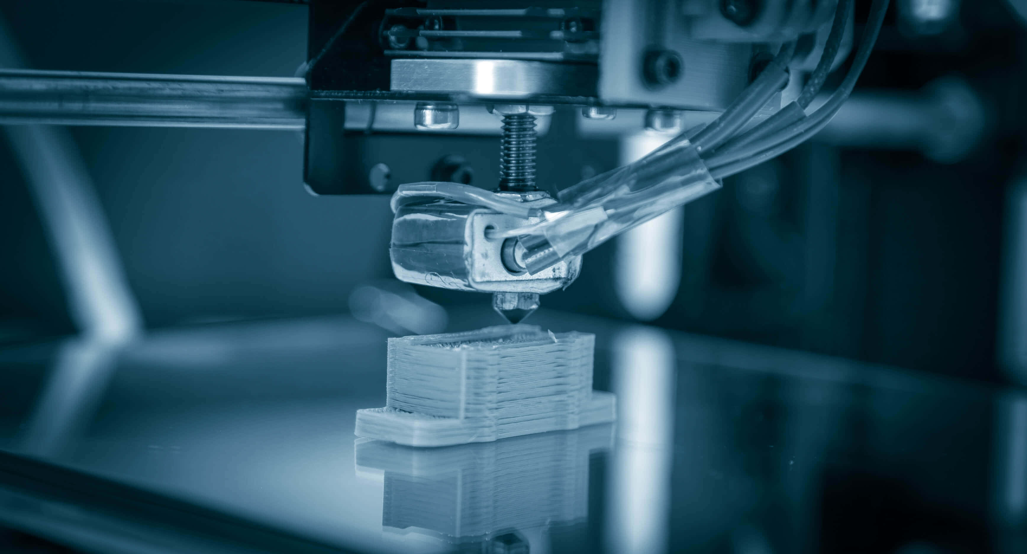 Manufacturing 桌布 壁紙 — 在冷藍色燈光下，3D列印機擠出線材以構建分層塑料物體的近距離特寫。