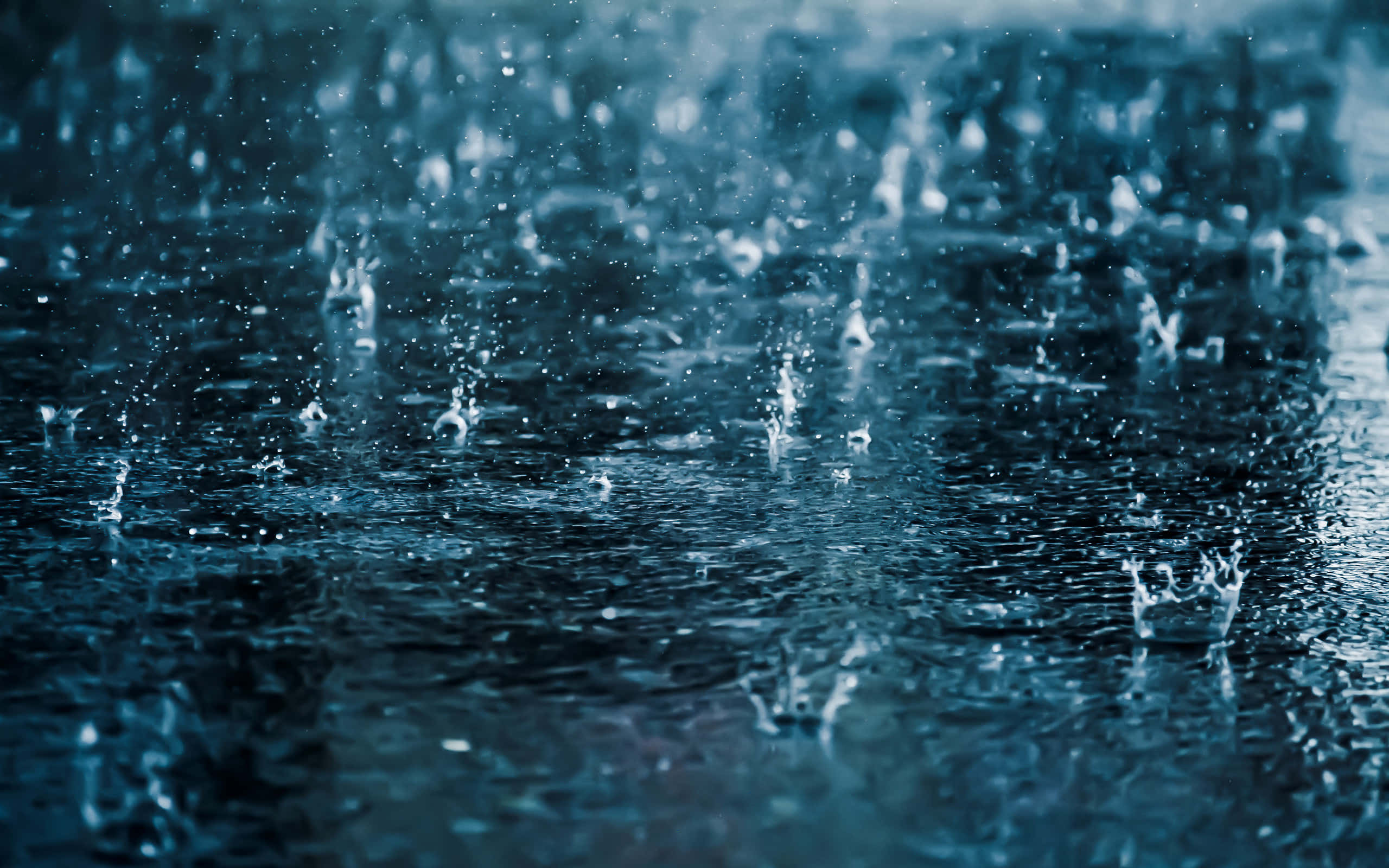 下雨 桌布 壁紙 — 在冷藍色燈光下，雨滴在黑暗潮濕的表面上飛濺並泛起漣漪。