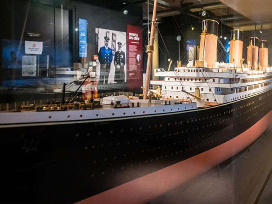 Titanic 桌布 壁紙 — 在博物館玻璃展櫃中展示的鐵達尼號詳細比例模型，背景有歷史海報。
