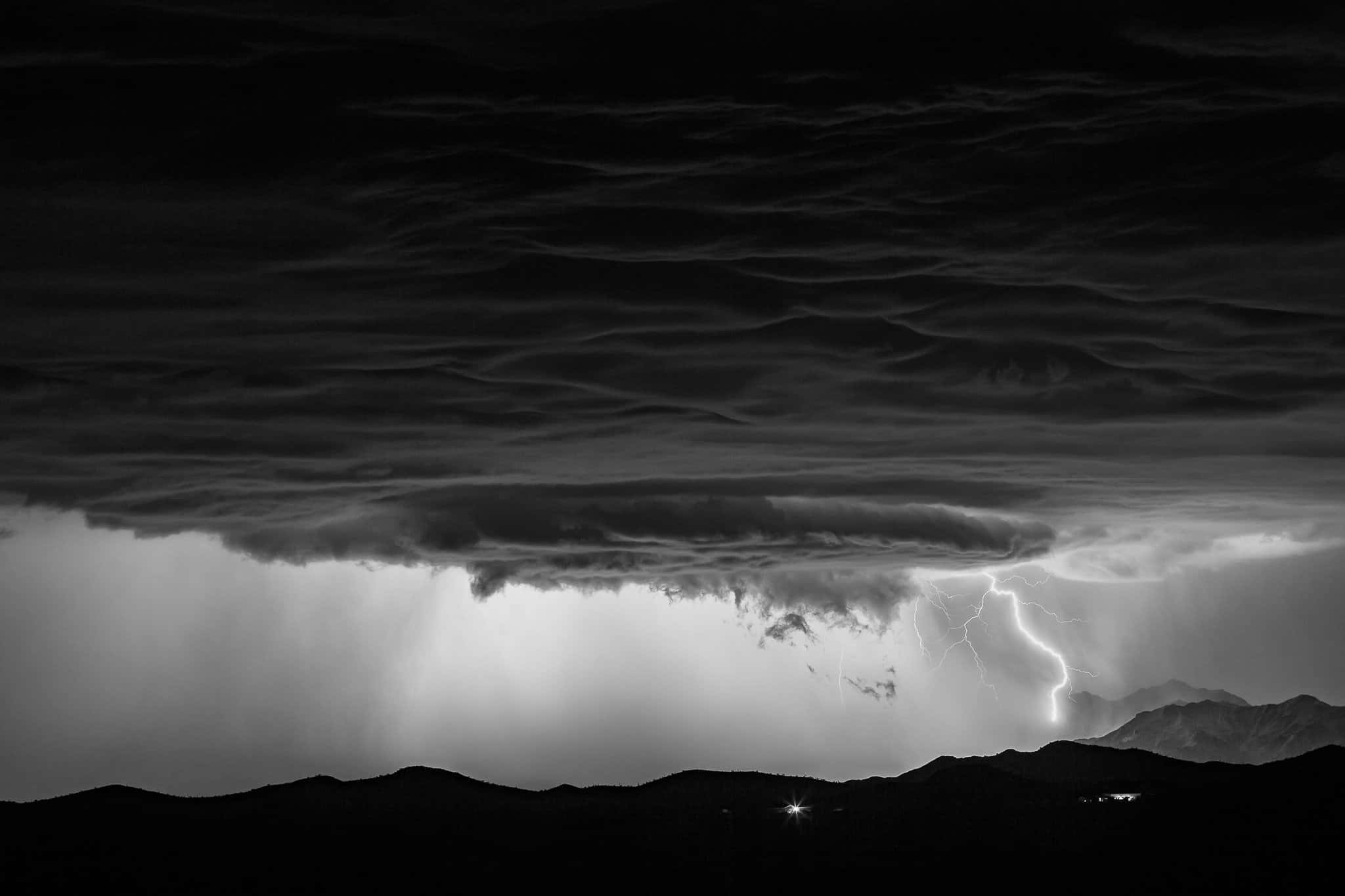Black And White Storm 桌布 壁紙 — 在厚重雲層下，閃電擊中剪影山脈的戲劇性黑白風暴。
