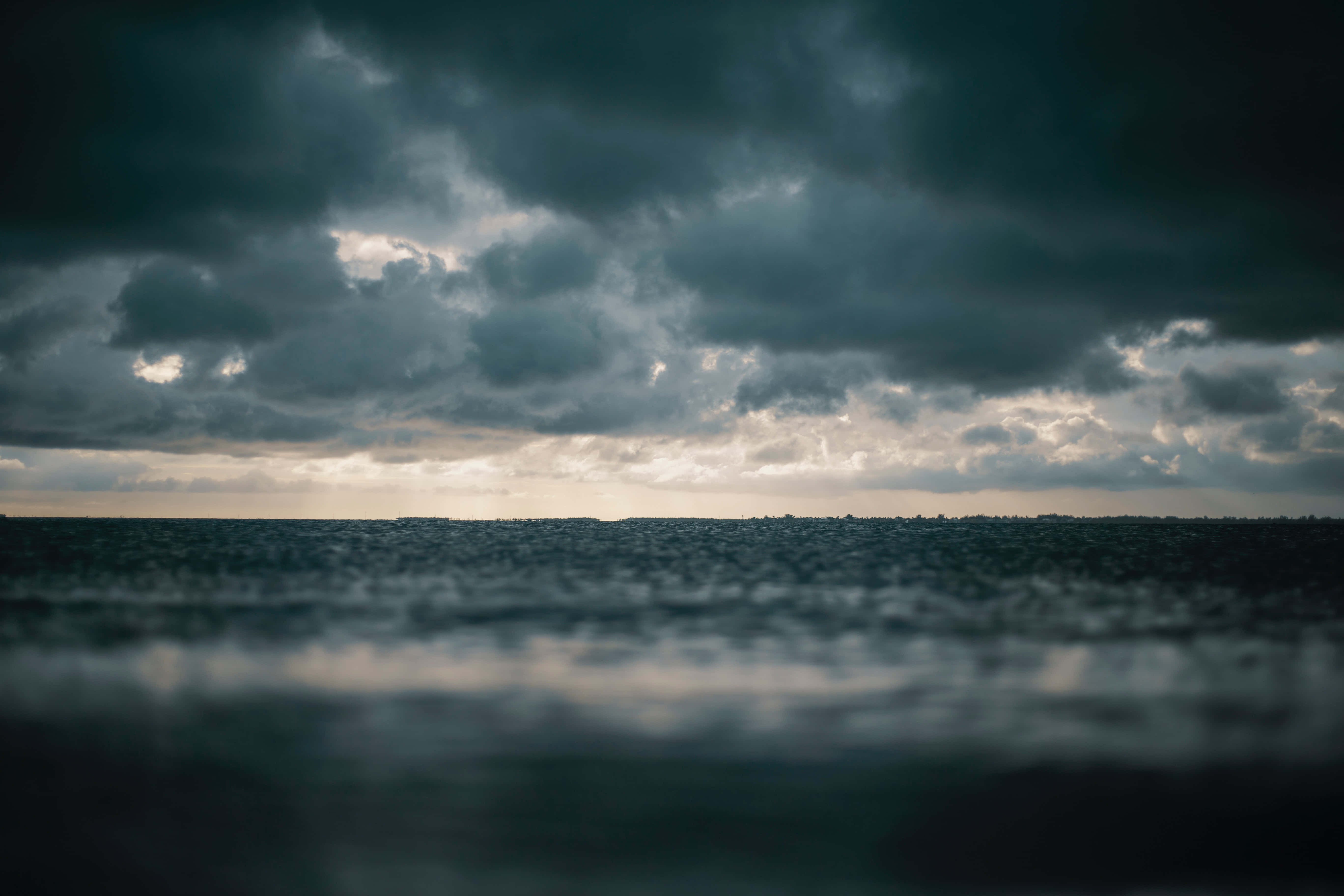 Dark Sky 桌布 壁紙 — 在厚重風暴雲下，陽光穿透地平線的陰鬱海景。