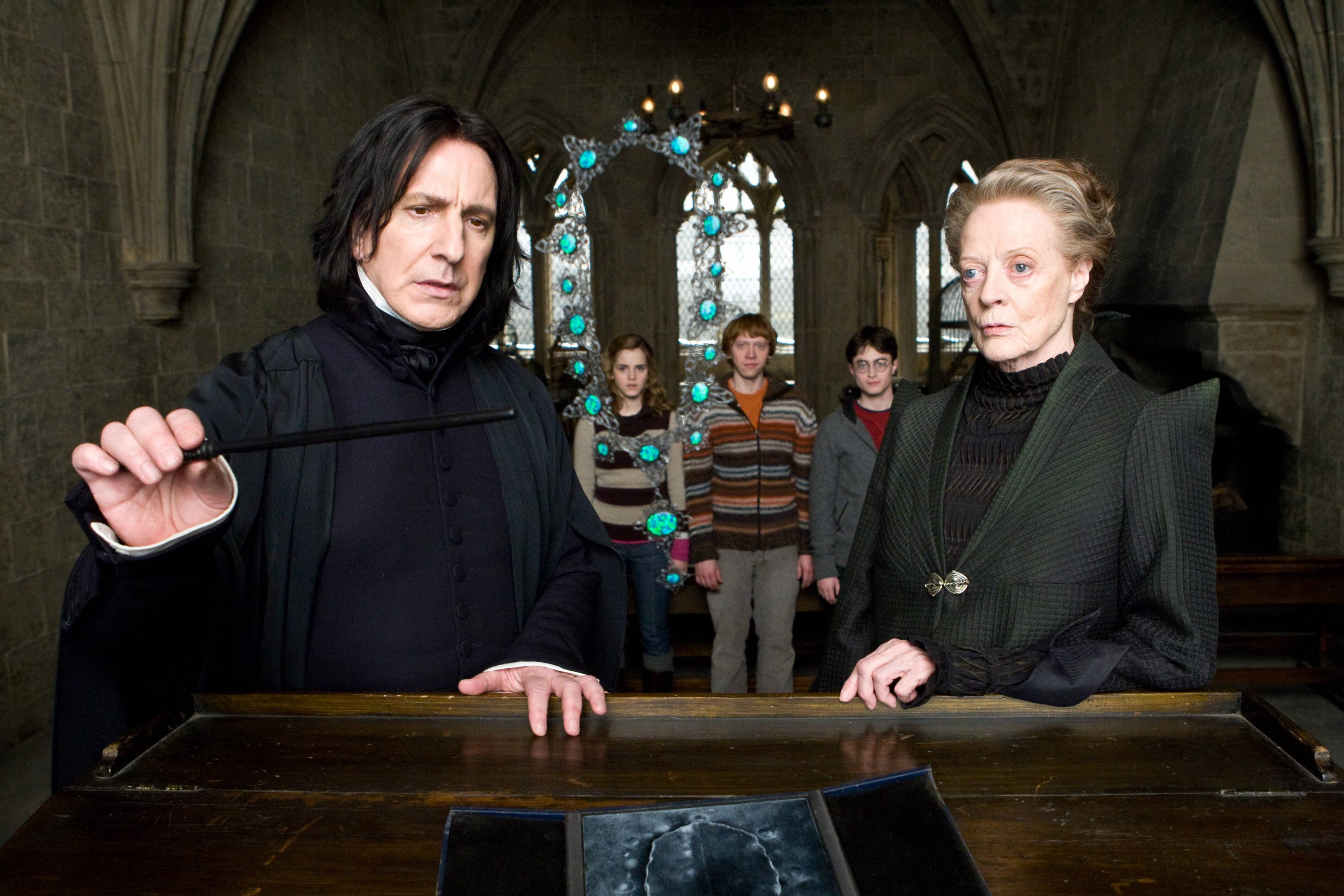 Severus Snape 桌布 壁紙 — 在哥德式石造大廳中，賽佛勒斯·石內卜和米奈娃·麥格站在一張木桌旁，身後有學生的戲劇性場景。