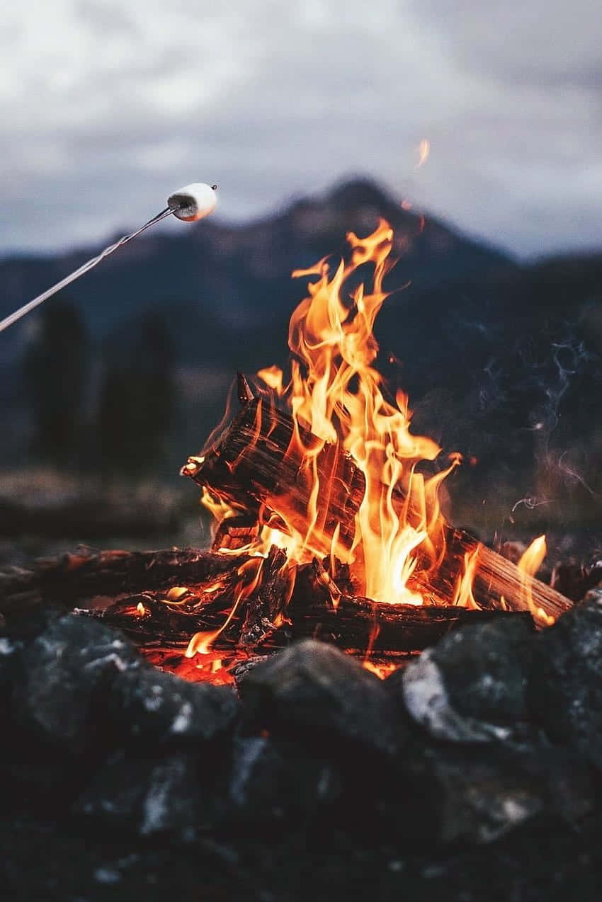 Fall Bonfire 桌布 壁紙 — 在噼啪作響的營火上烤著棉花糖，背景是煙霧繚繞的山脈。