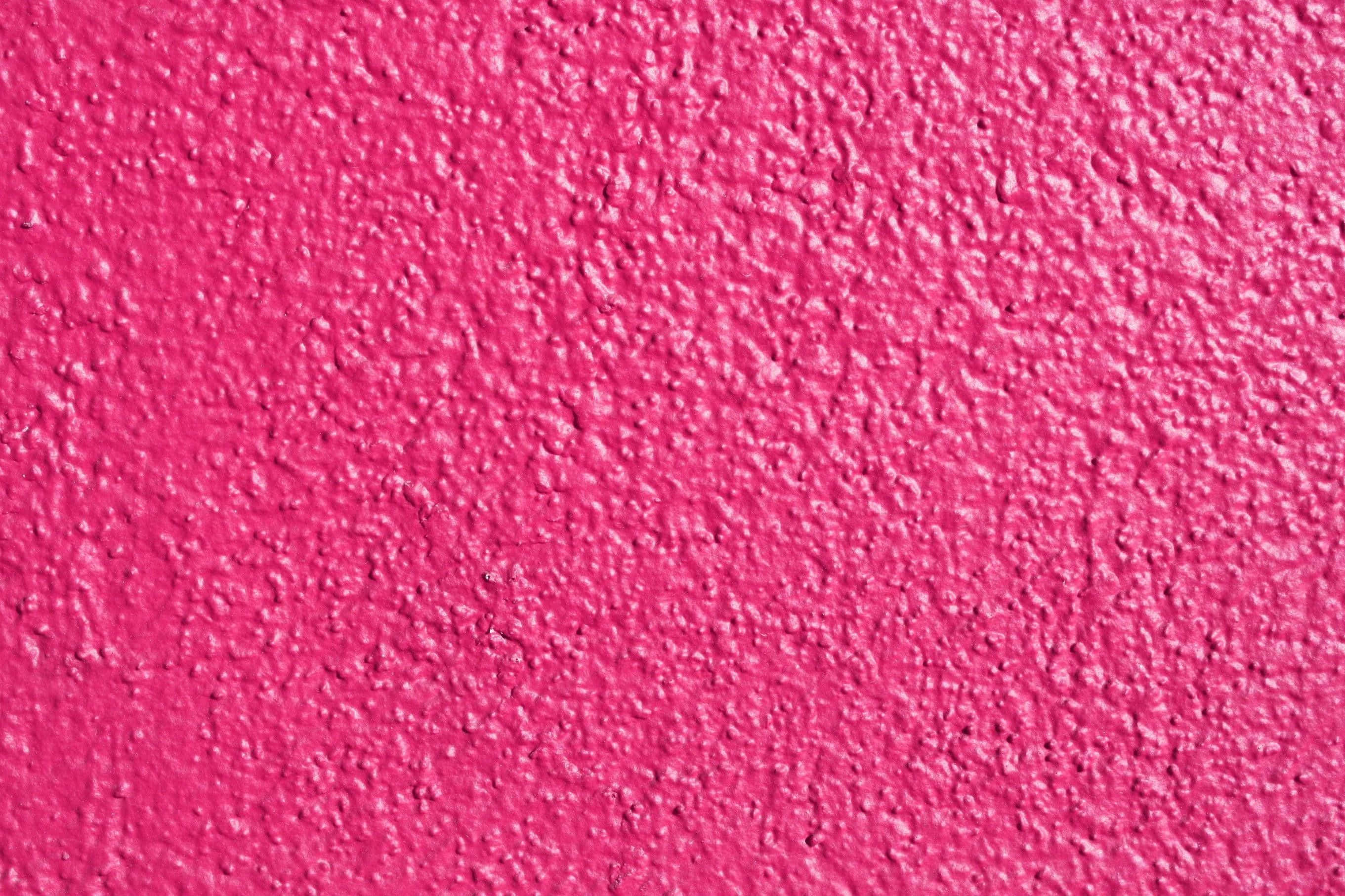 Pink Texture 桌布 壁紙 — 在均勻照明下，帶有粗糙卵石飾面的鮮豔粉紅色紋理牆面。