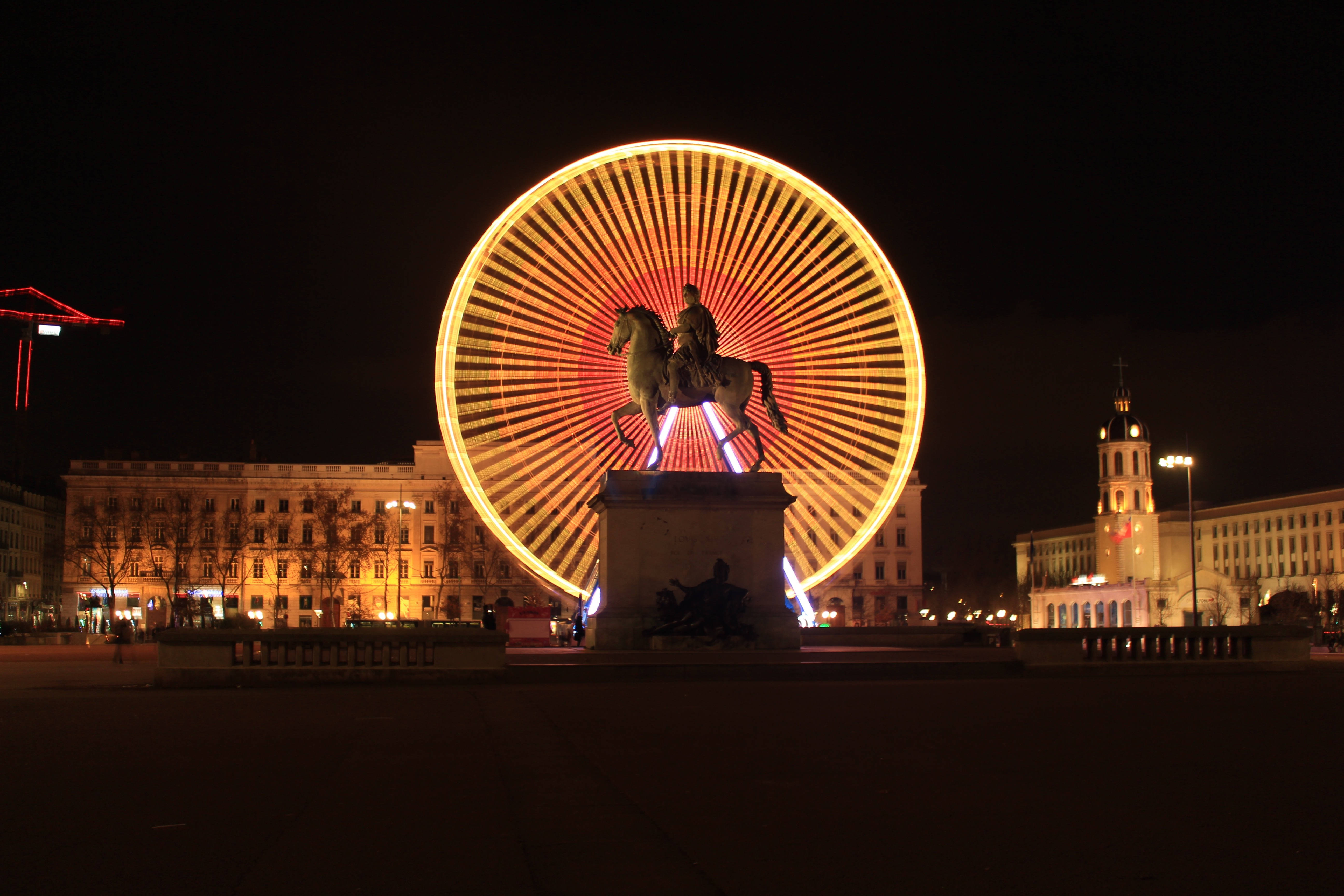France 桌布 壁紙 — 在夜晚的城市廣場上，一個發光的摩天輪在黑暗的騎馬雕像後方散發出溫暖的光芒。