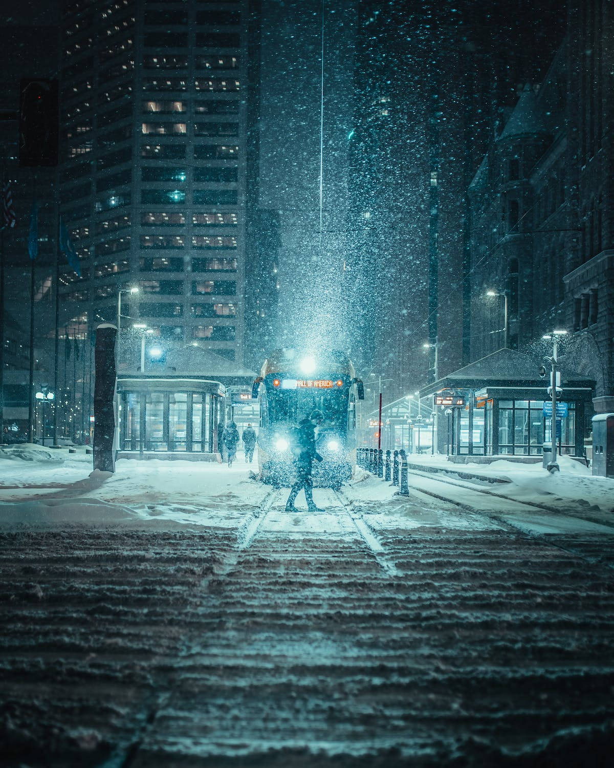 城市 桌布 壁紙 — 在夜晚霓虹燈照亮的城市中，一個孤獨的身影在飄雪中走向一輛積雪的電車。