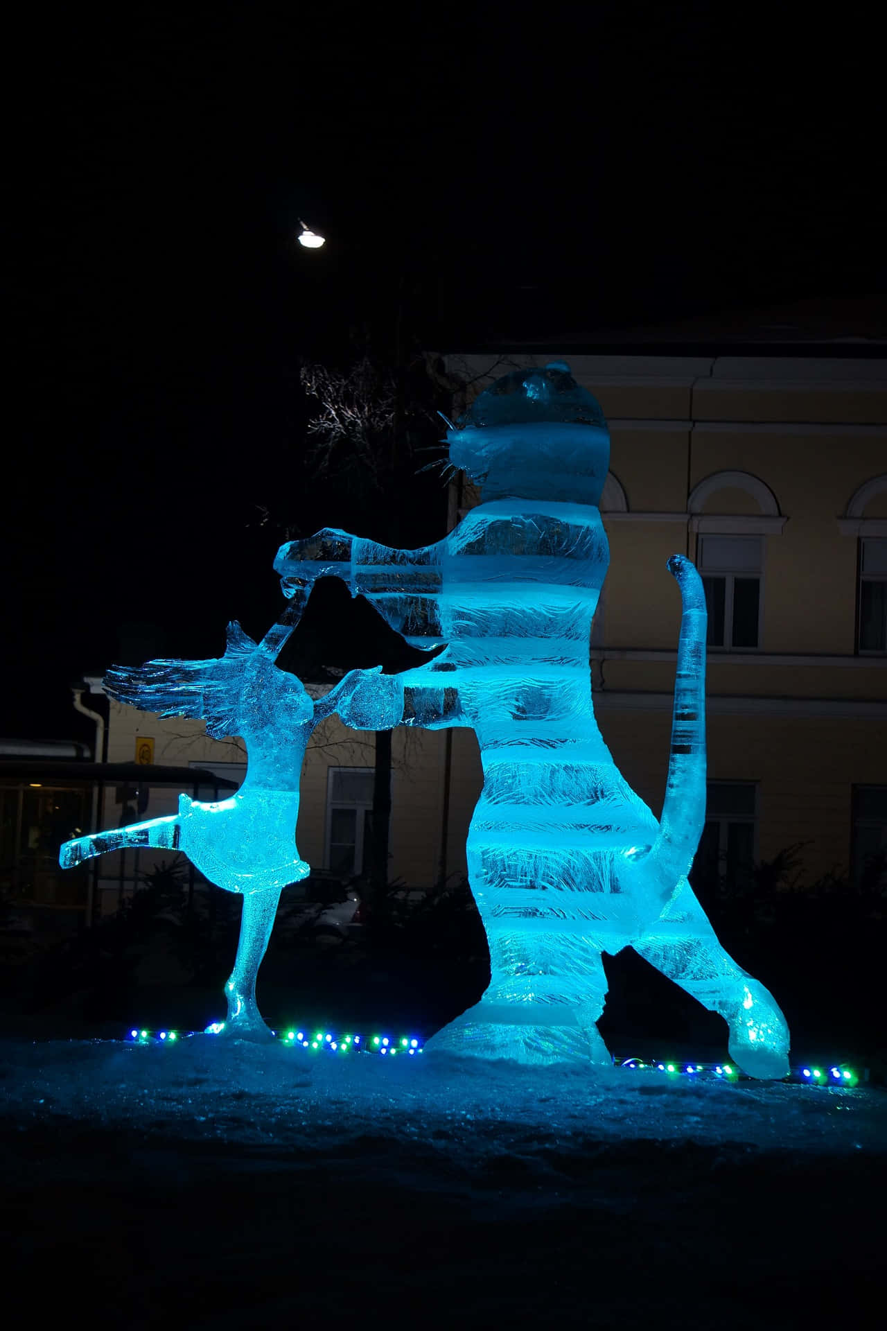 Ice Sculpture 桌布 壁紙 — 在夜晚黑暗建築背景下，發光的藍色冰雕，描繪跳舞的女孩和老虎。