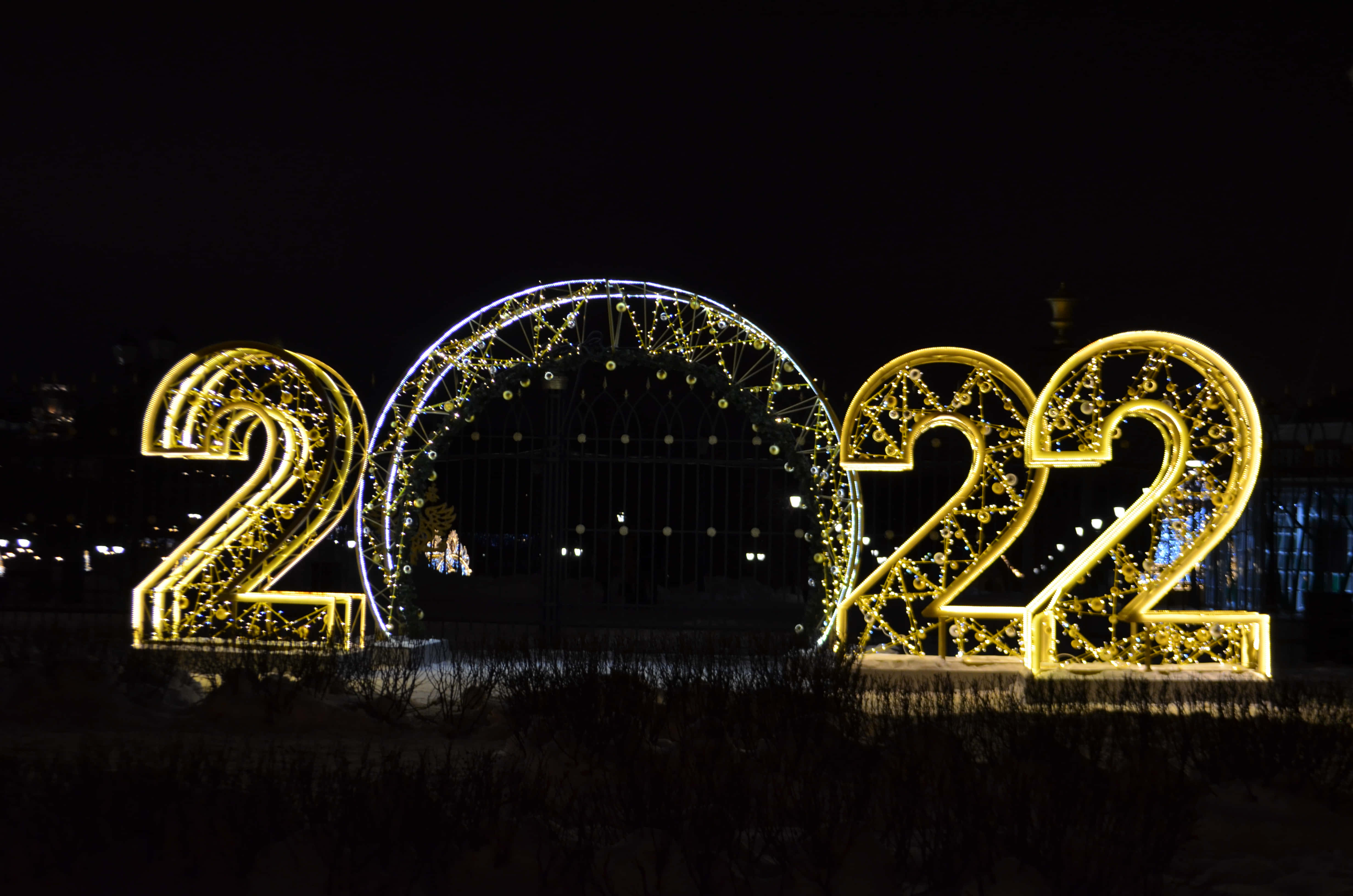 2022 桌布 壁紙 — 在夜間，發光的金色 '2022' 數字和拱門在黑暗的天空和遠處的城市燈光下照亮。