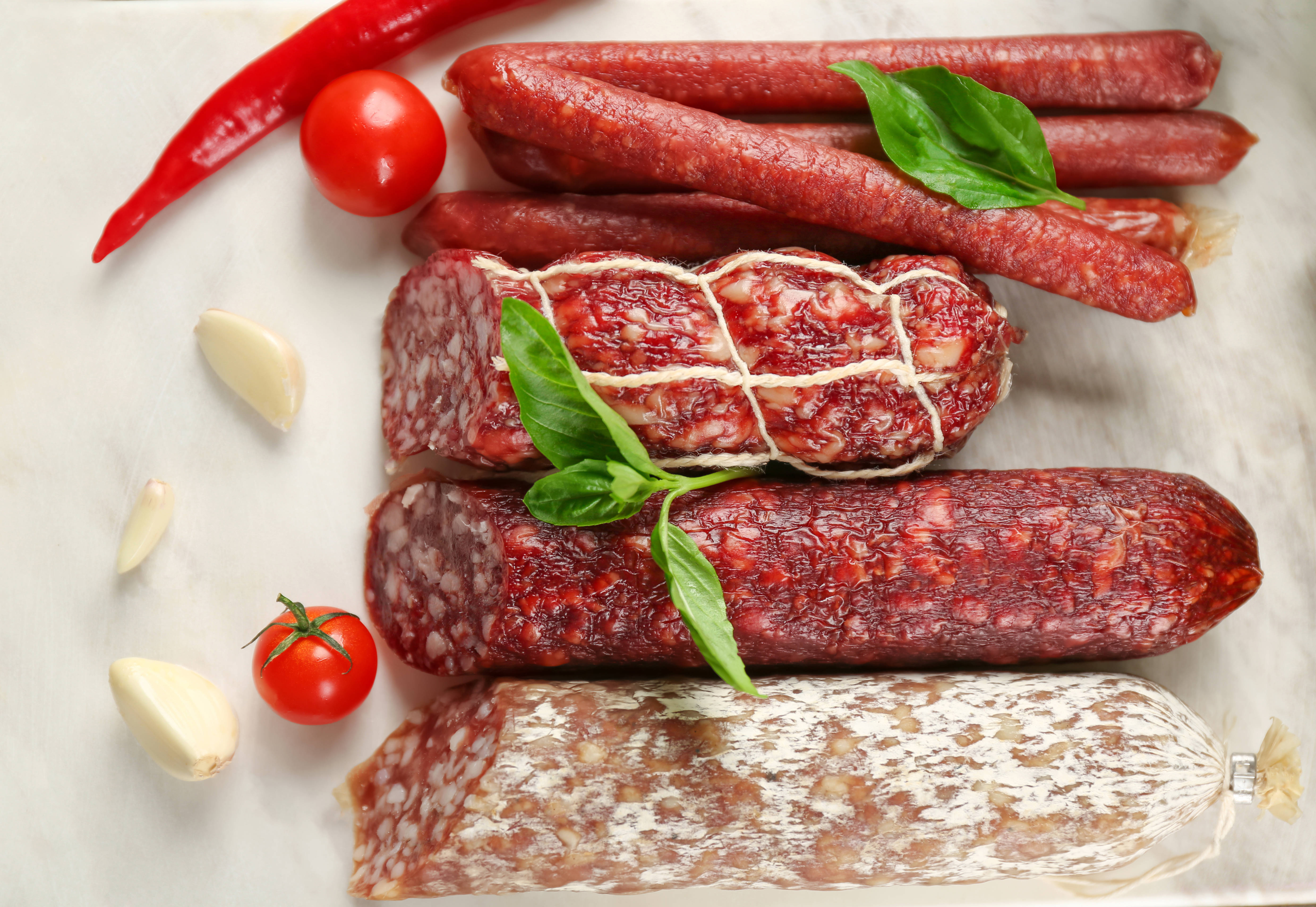 meat 桌布 壁紙 — 在大理石表面上擺放各種醃製香腸，並以羅勒番茄和蒜瓣裝飾的平鋪佈置。